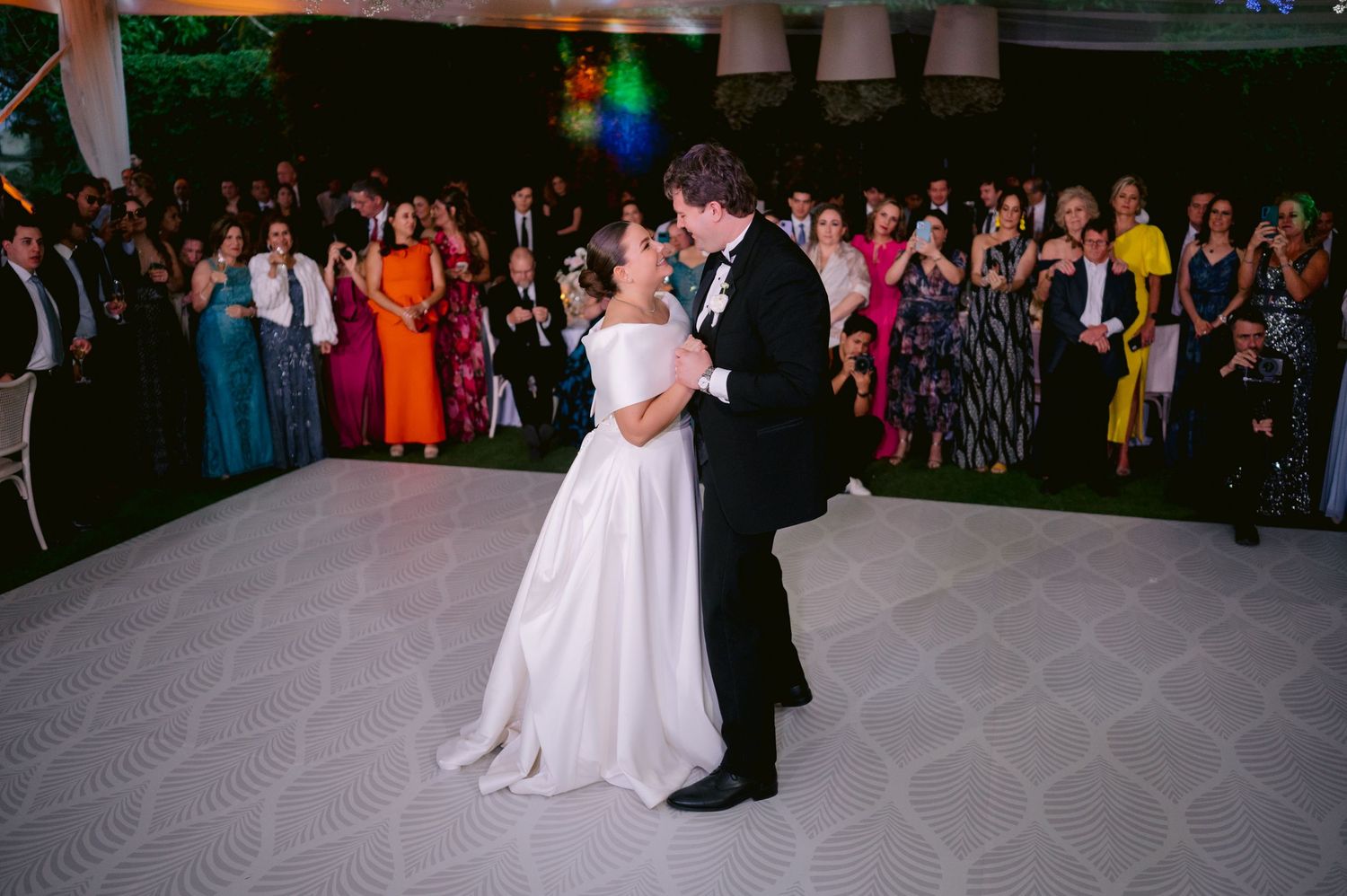 Wedding couple dances surrounded by guests under twinkling lights in a stunning reception setting.