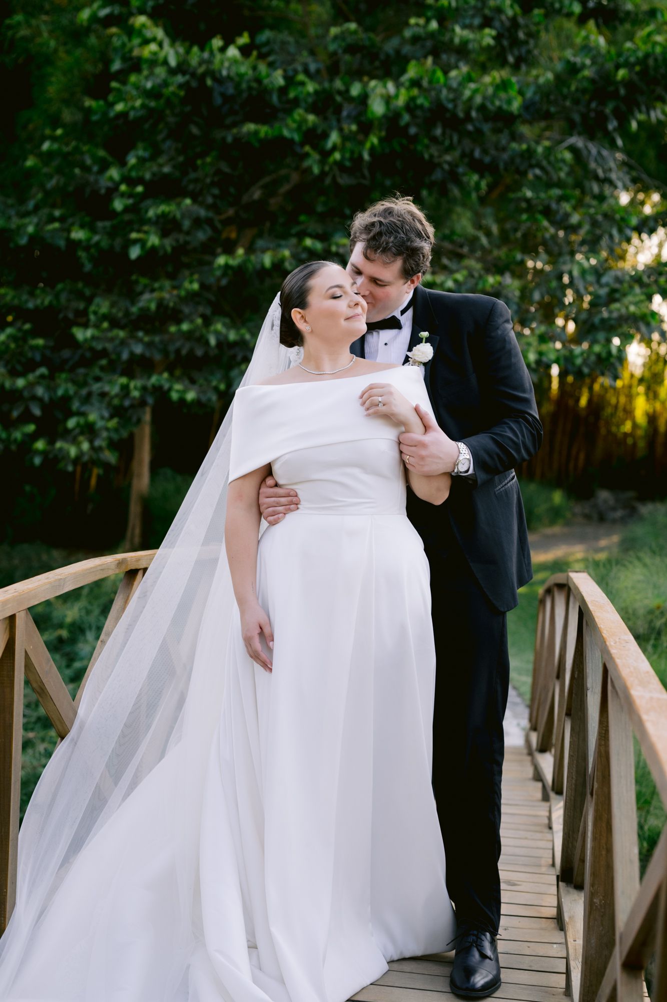 A joyful wedding moment captured on a wooden bridge with lush greenery in the background.