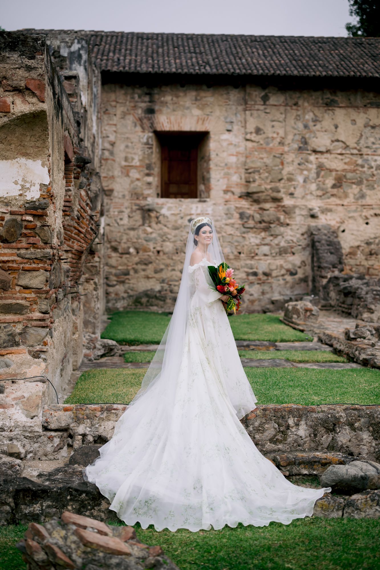 Full-length bridal portrait with colorful bouquet and dramatic train against historic architecture.