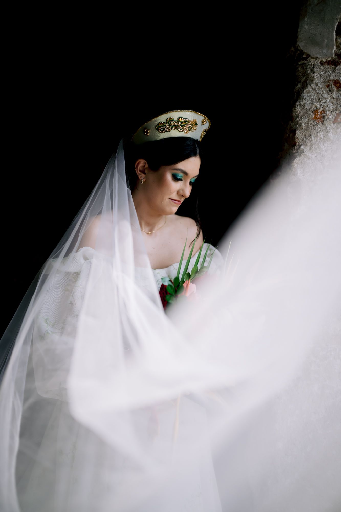 Artistic bridal portrait with flowing white veil against dark backdrop.