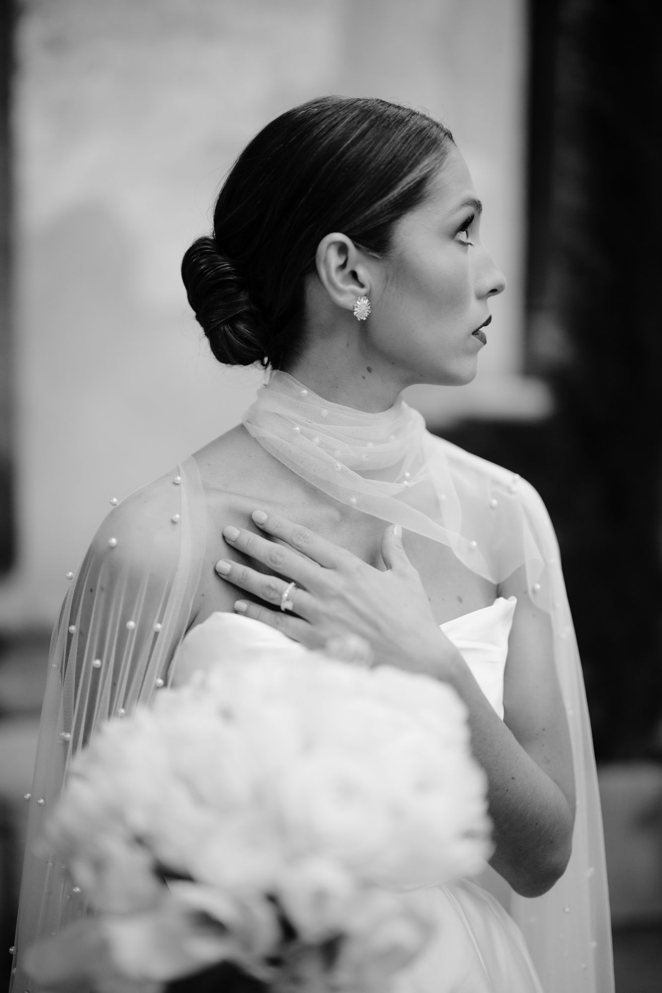 Classic black and white profile portrait of bride with elegant updo and pearl-adorned cape.