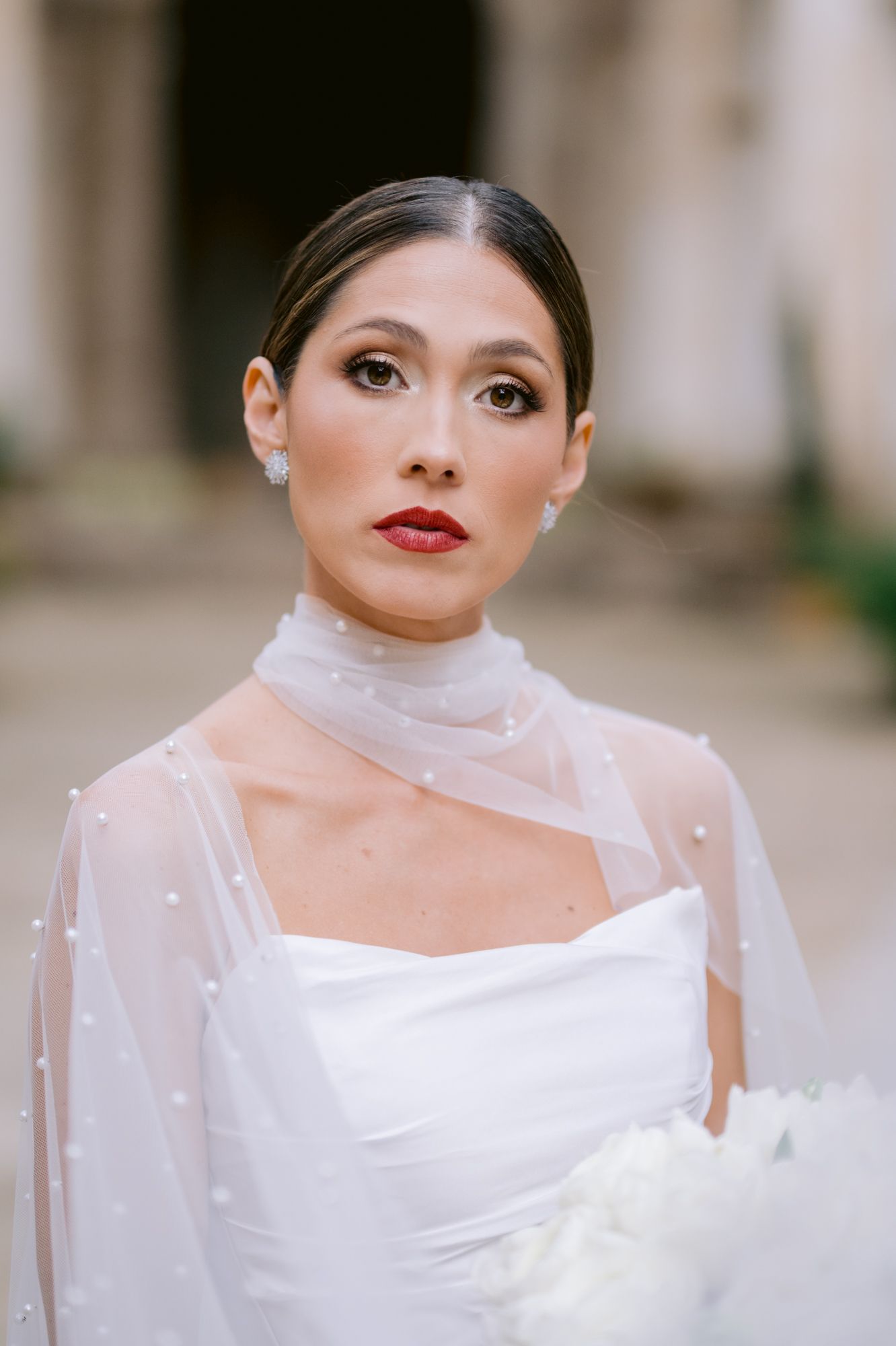 Elegant bride wearing classic white dress and sheer high-neck overlay with red lipstick and polished updo.