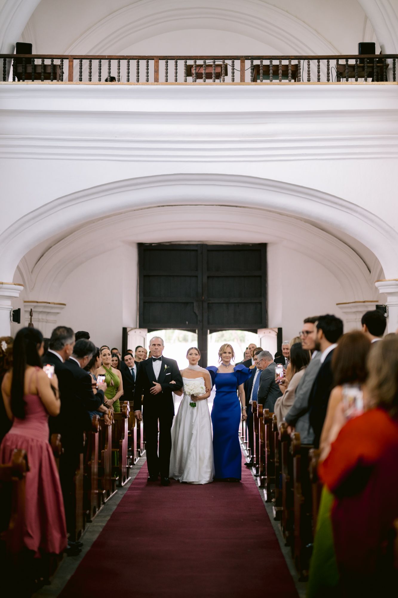 Wedding ceremony processional in classic white church interior with red carpet aisle.