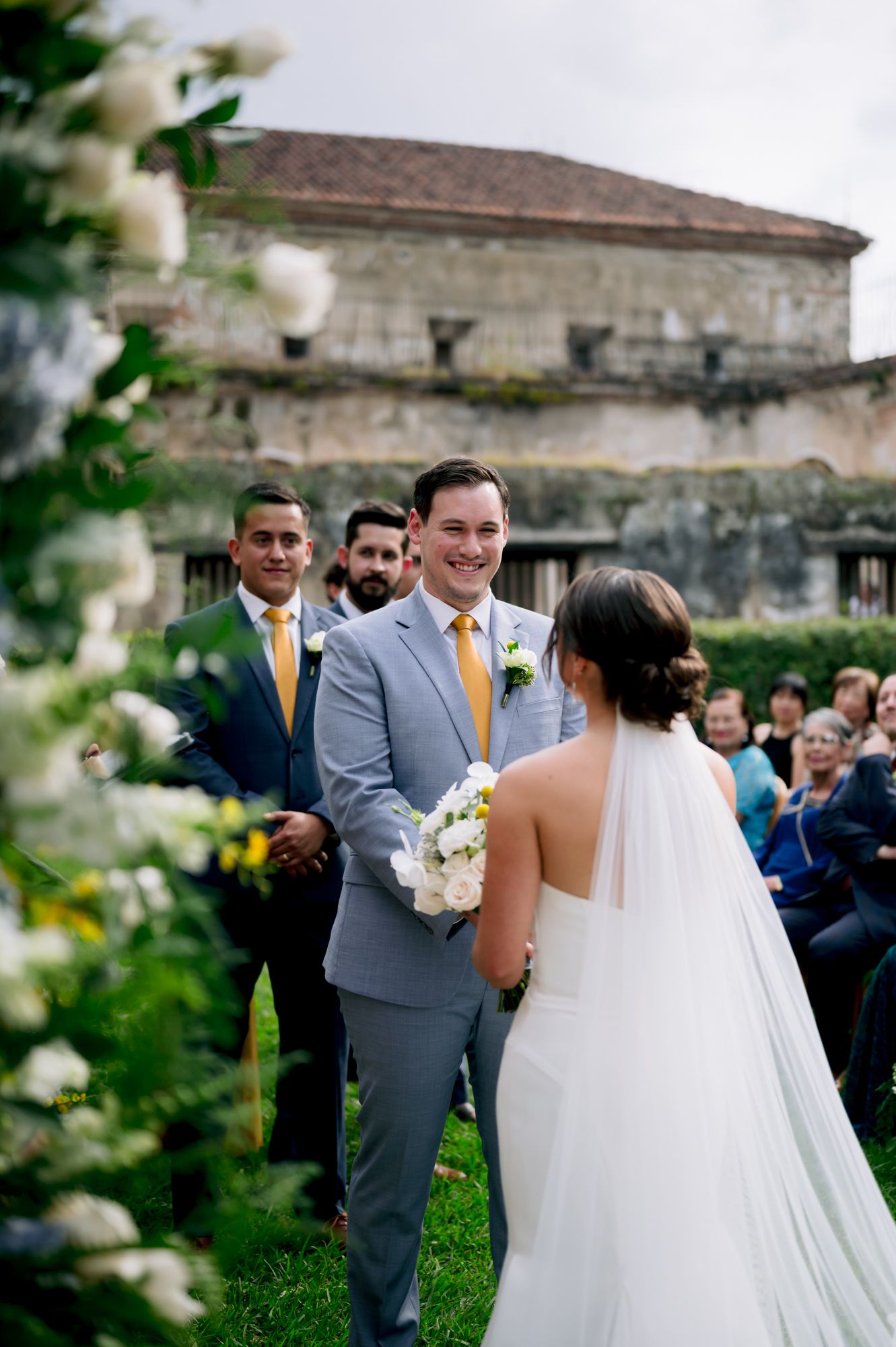 Wedding ceremony in a historic courtyard with stone walls and green lawn.
