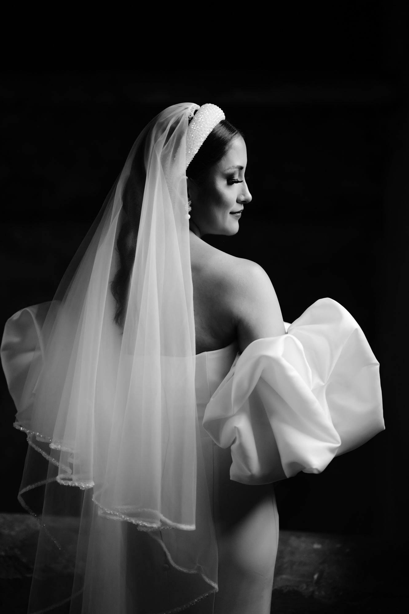 Elegant black and white profile portrait of bride with flowing veil and statement sleeve.