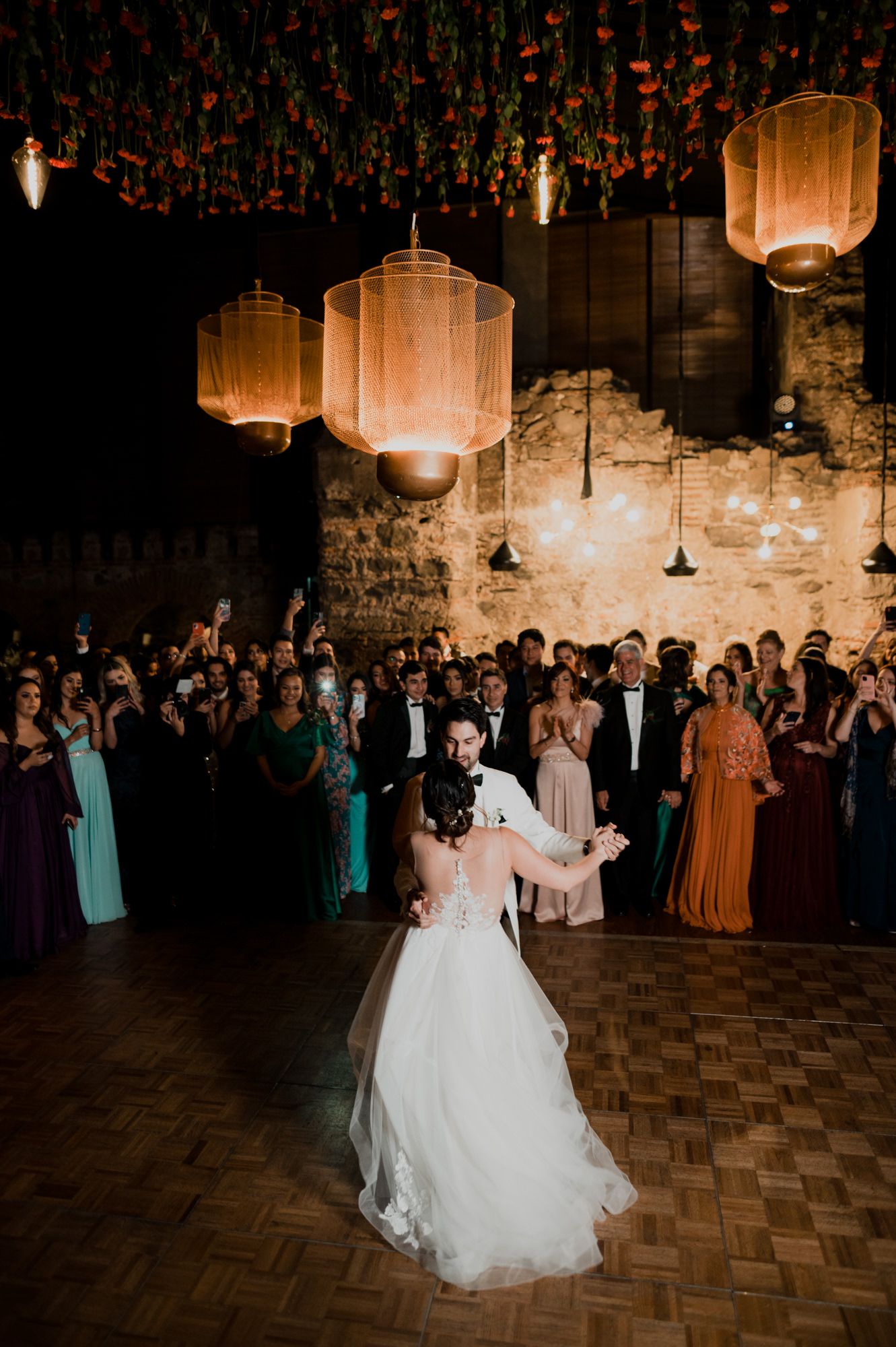 Couple sharing their first dance under illuminated lanterns and floral ceiling decorations at wedding reception.