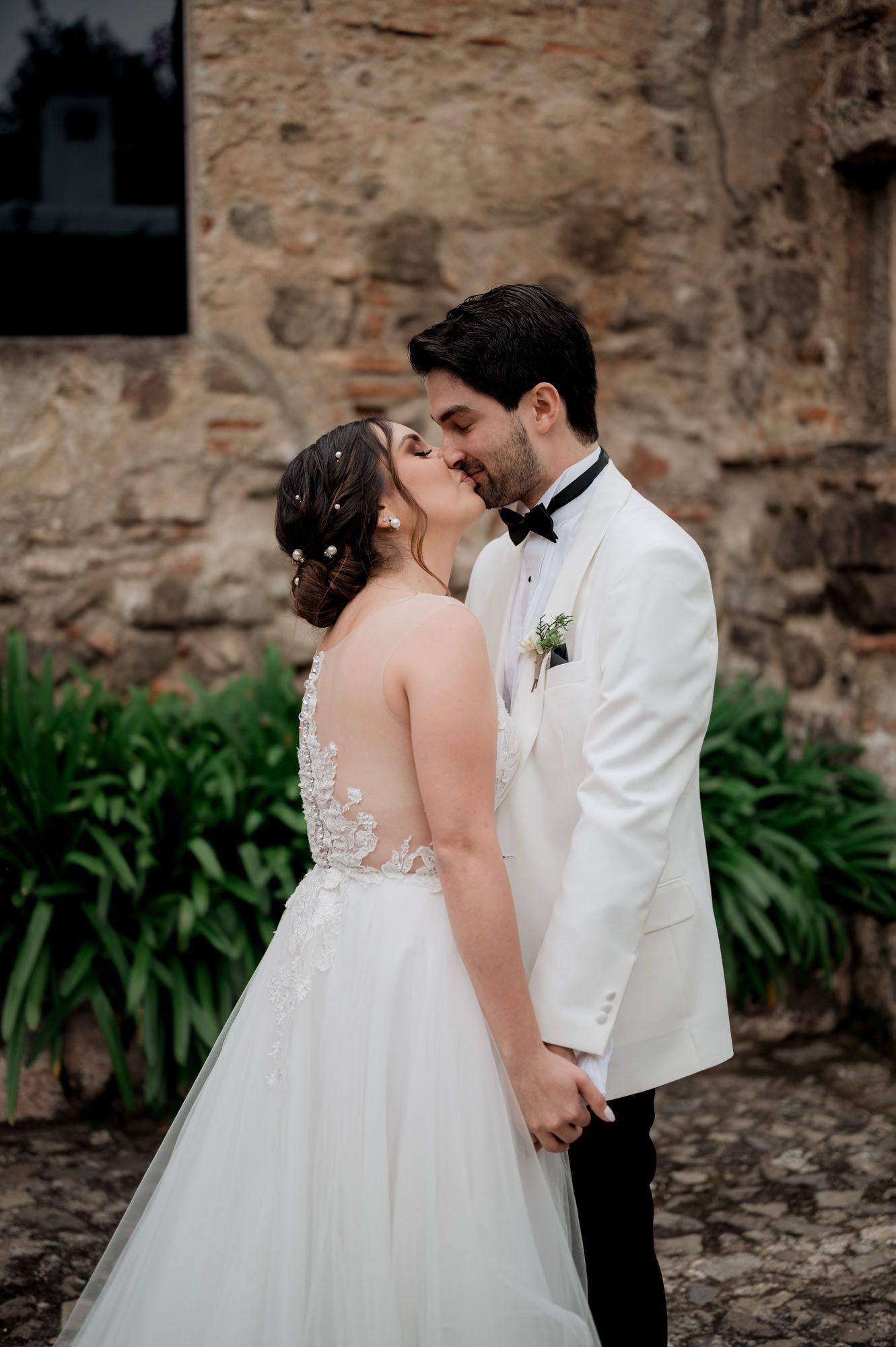 Romantic wedding kiss captured against historic stone wall backdrop.
