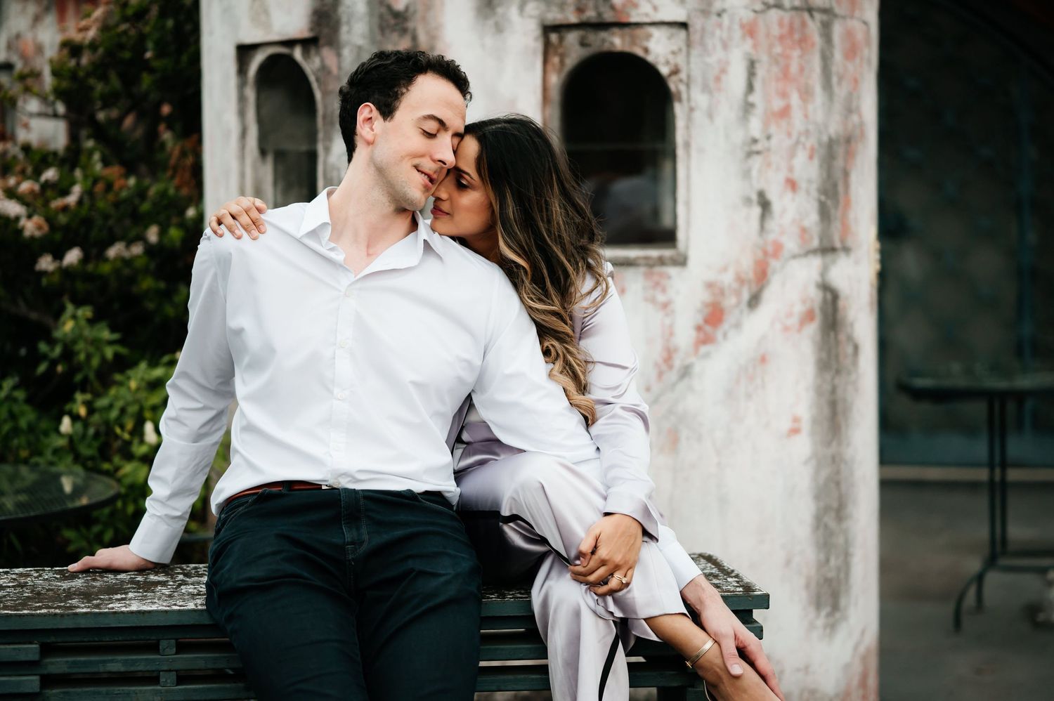 A romantic couple embracing on a rustic bench in front of an old building.