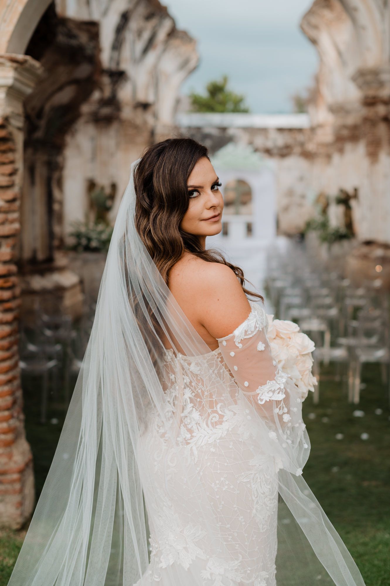 Elegant bridal portrait showcasing a delicate lace wedding gown with sheer details against historic ruins.