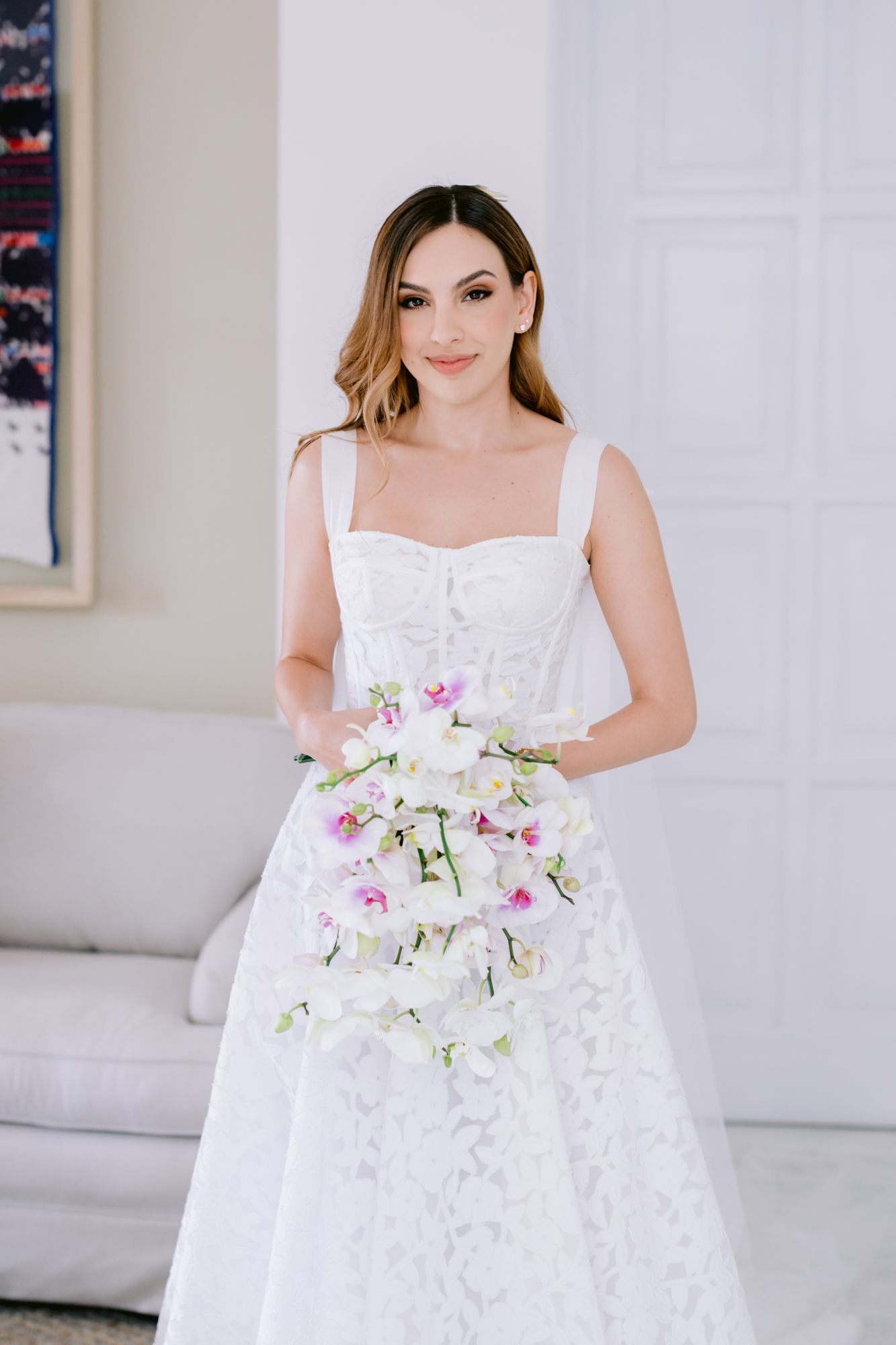 Elegant white lace wedding dress with delicate orchid bouquet in natural light.