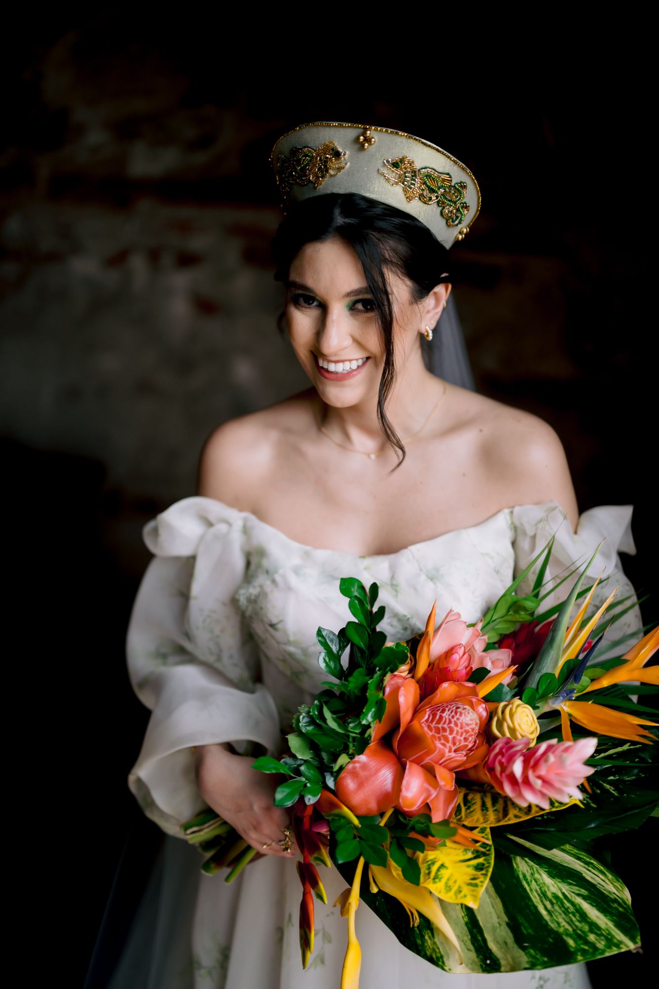 Bride in off-shoulder dress wearing nautical cap and holding tropical flower bouquet.