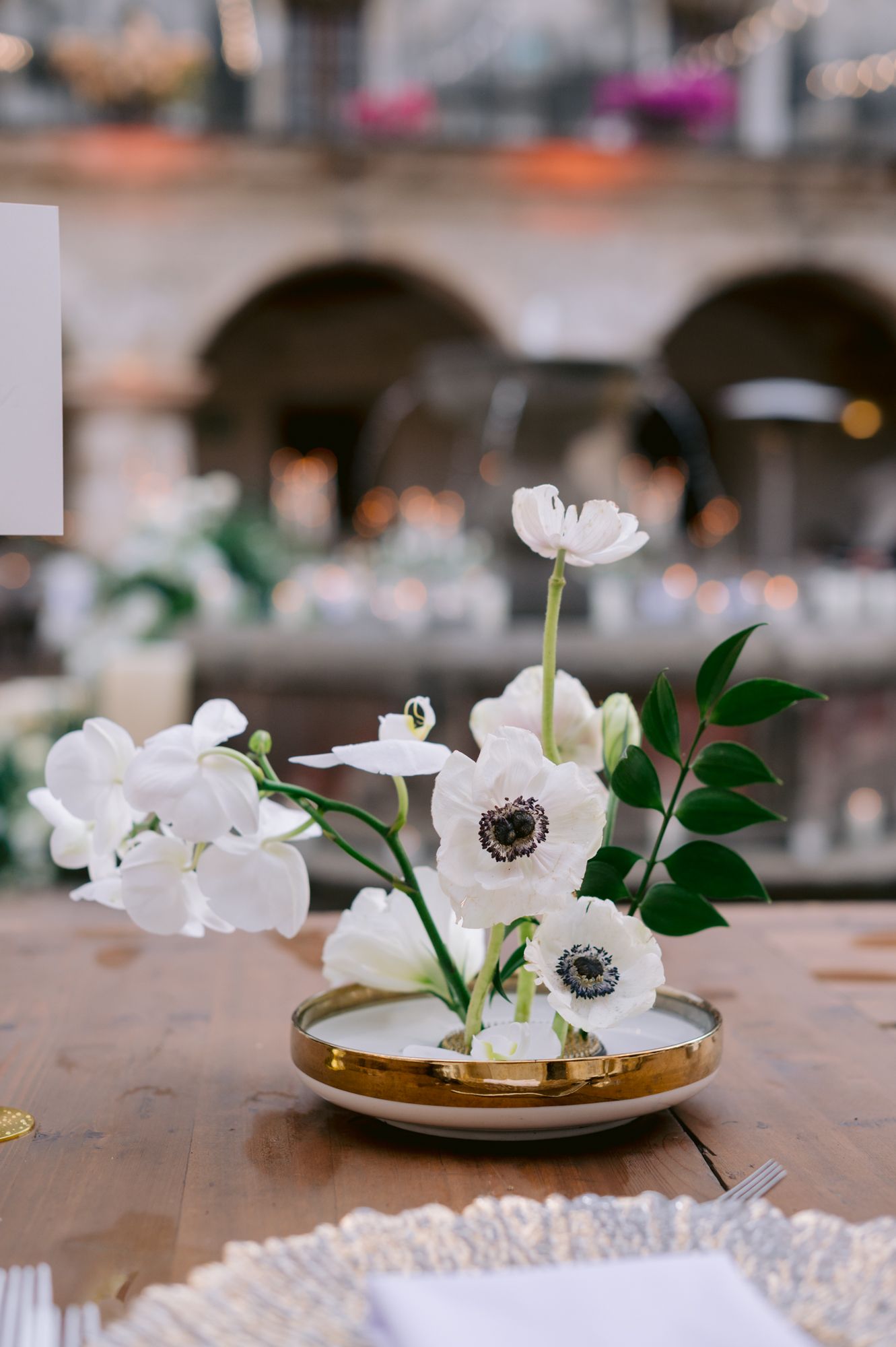 Delicate white anemone flowers arranged in gold-rimmed dish on wooden table.