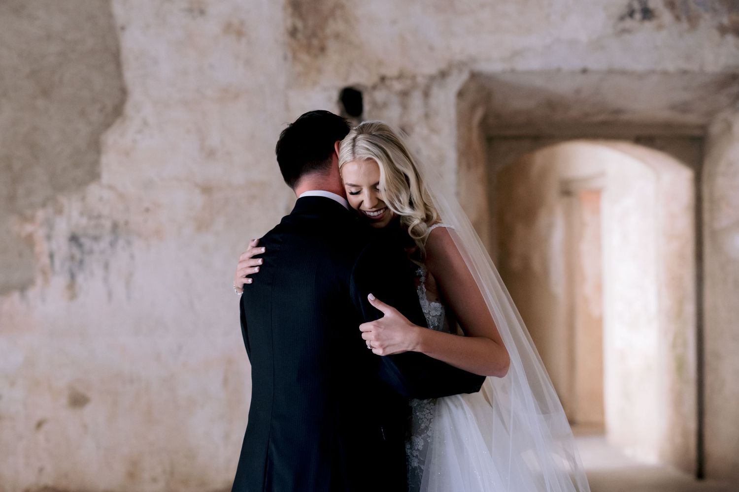 A romantic embrace between newlyweds in a rustic stone corridor with weathered walls.