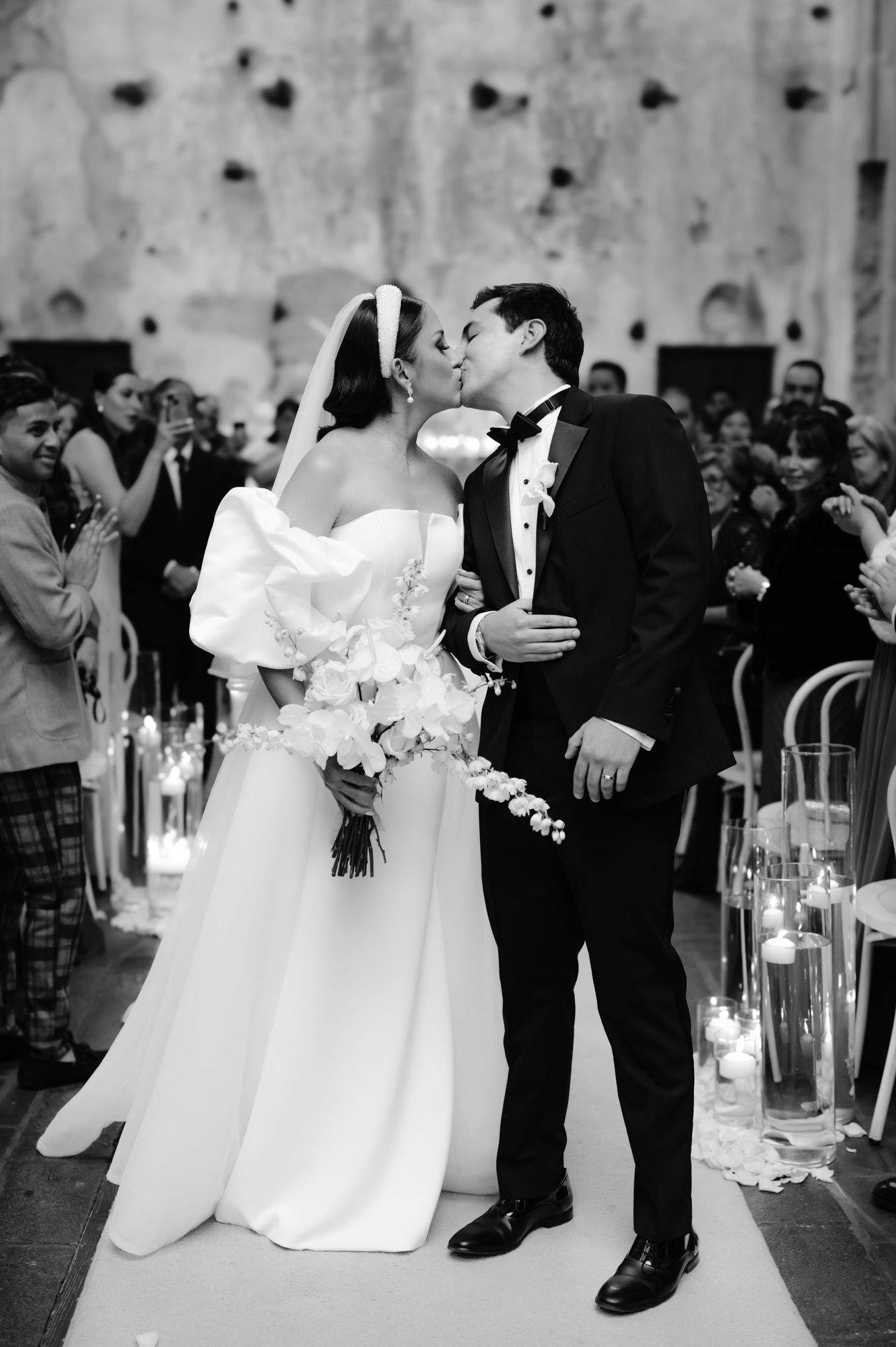Black and white wedding photo of first kiss with candle-lined aisle.