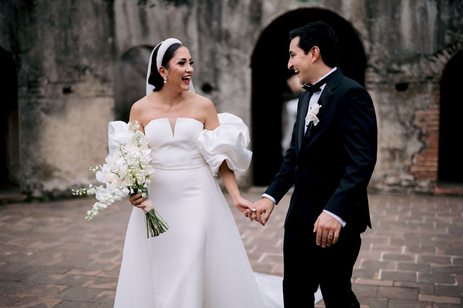 Wedding couple shares joyful moment against rustic stone wall backdrop.