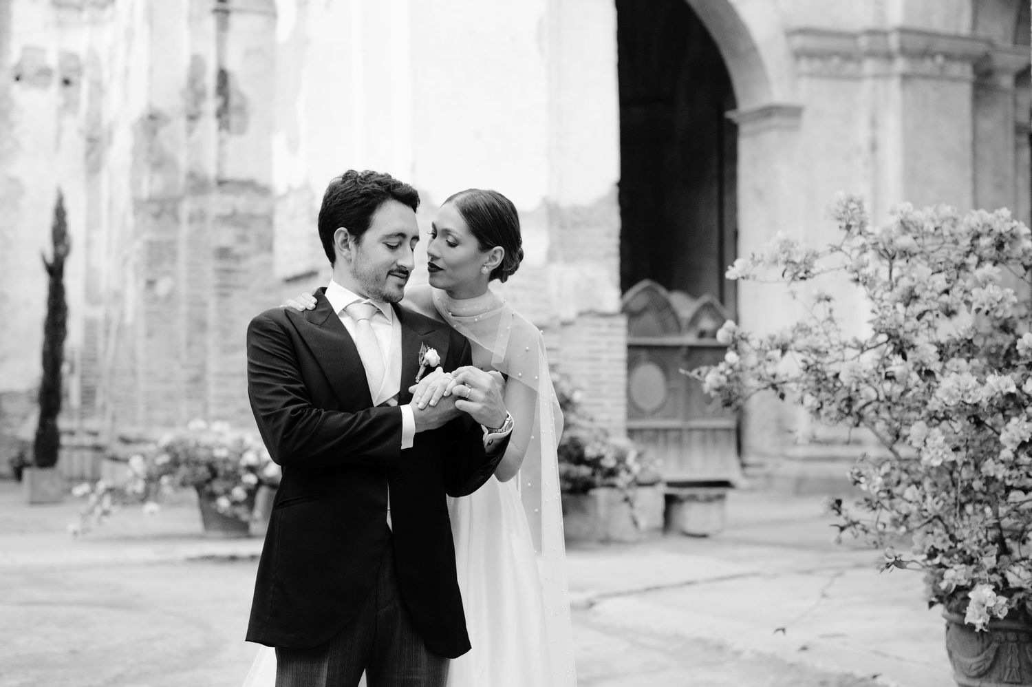 Black and white intimate moment between newlyweds in historic church courtyard.