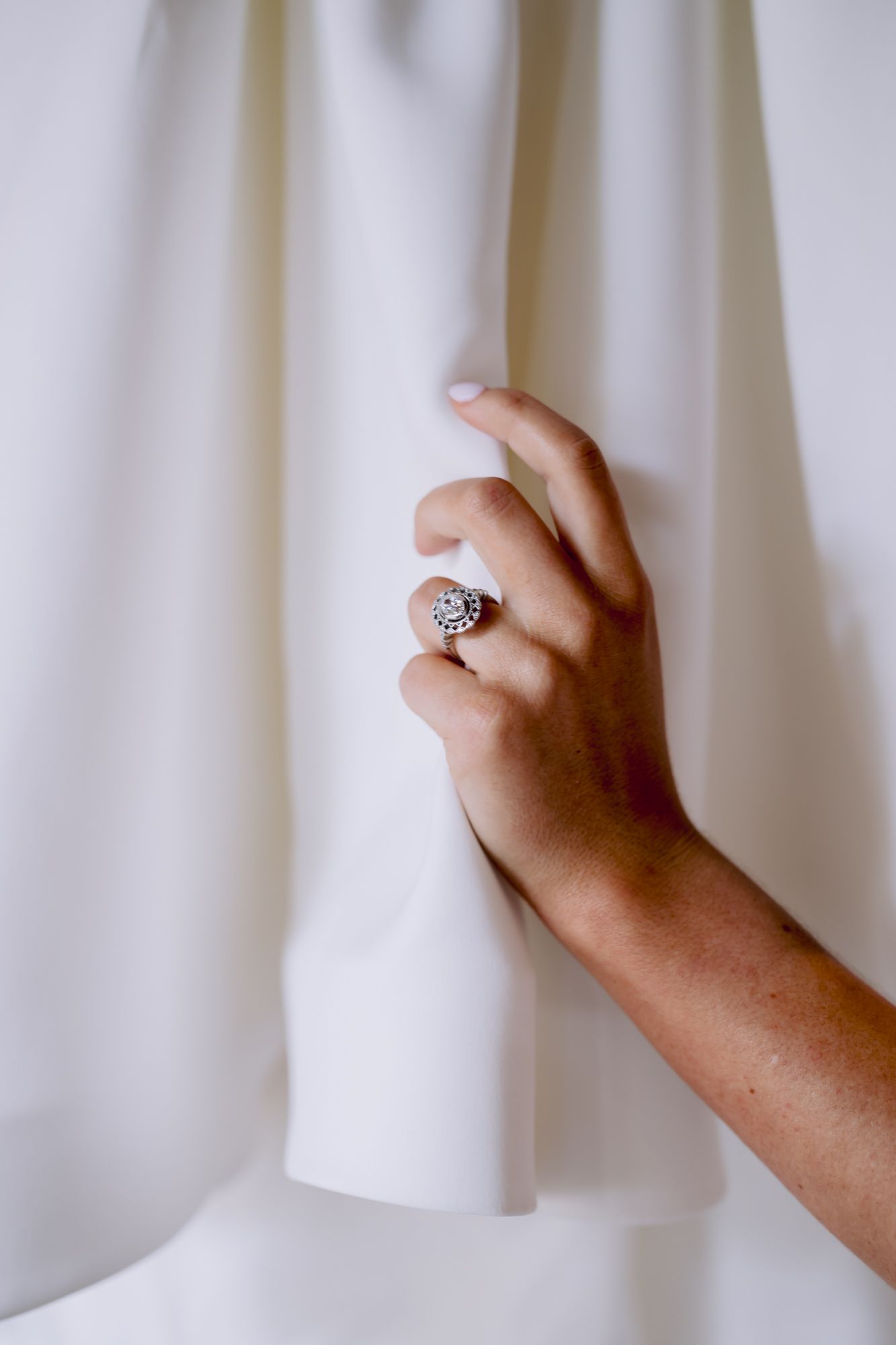 Close-up of hand wearing vintage-style engagement ring against white fabric.