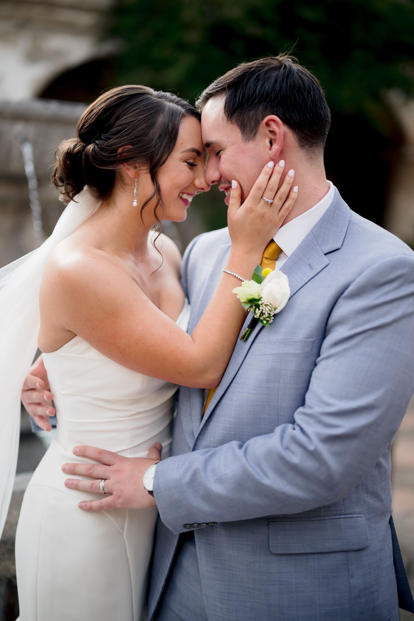 A tender wedding moment captured as a couple in formal attire embrace against a garden backdrop.