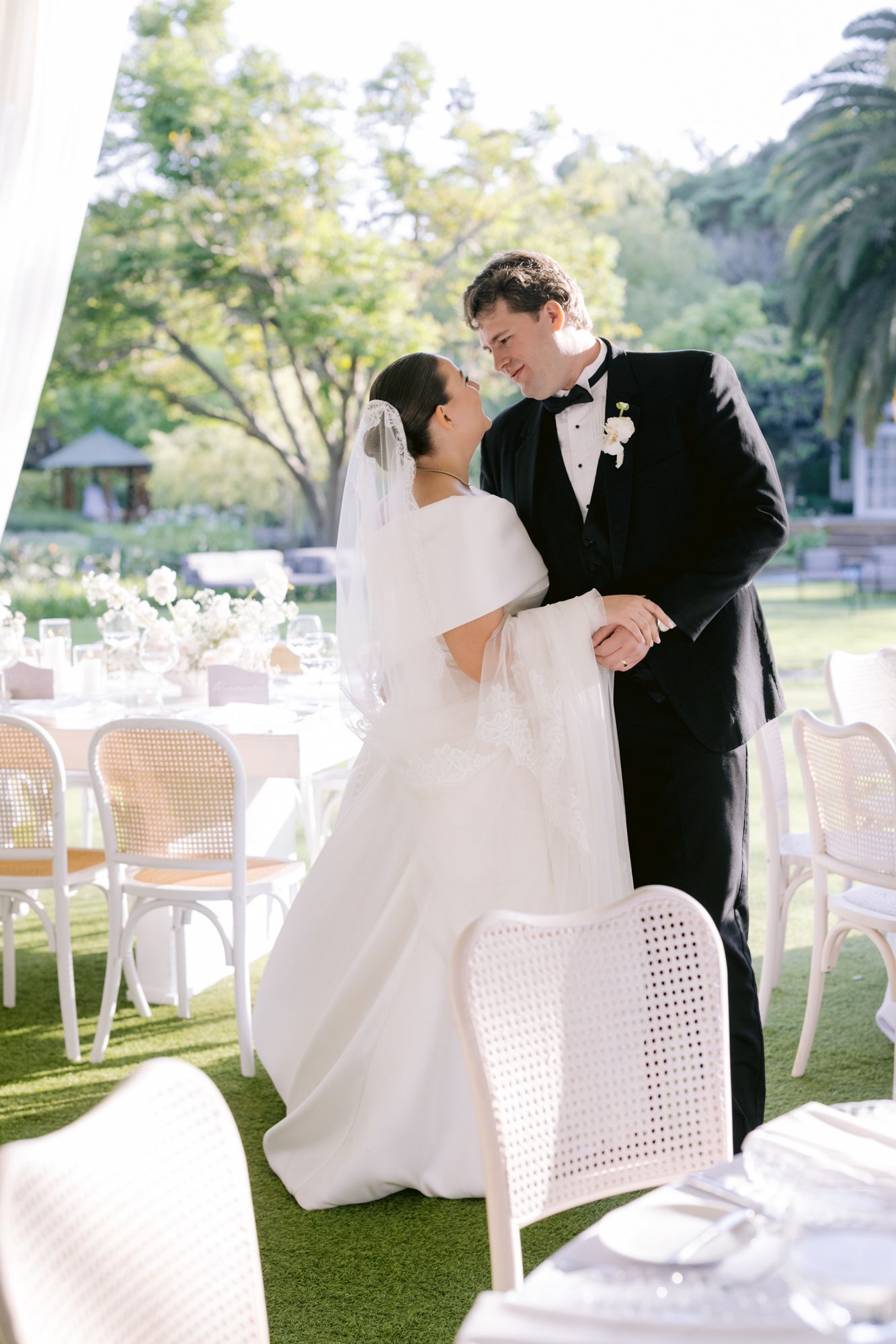 Intimate moment between newlyweds at outdoor wedding reception with white chairs.