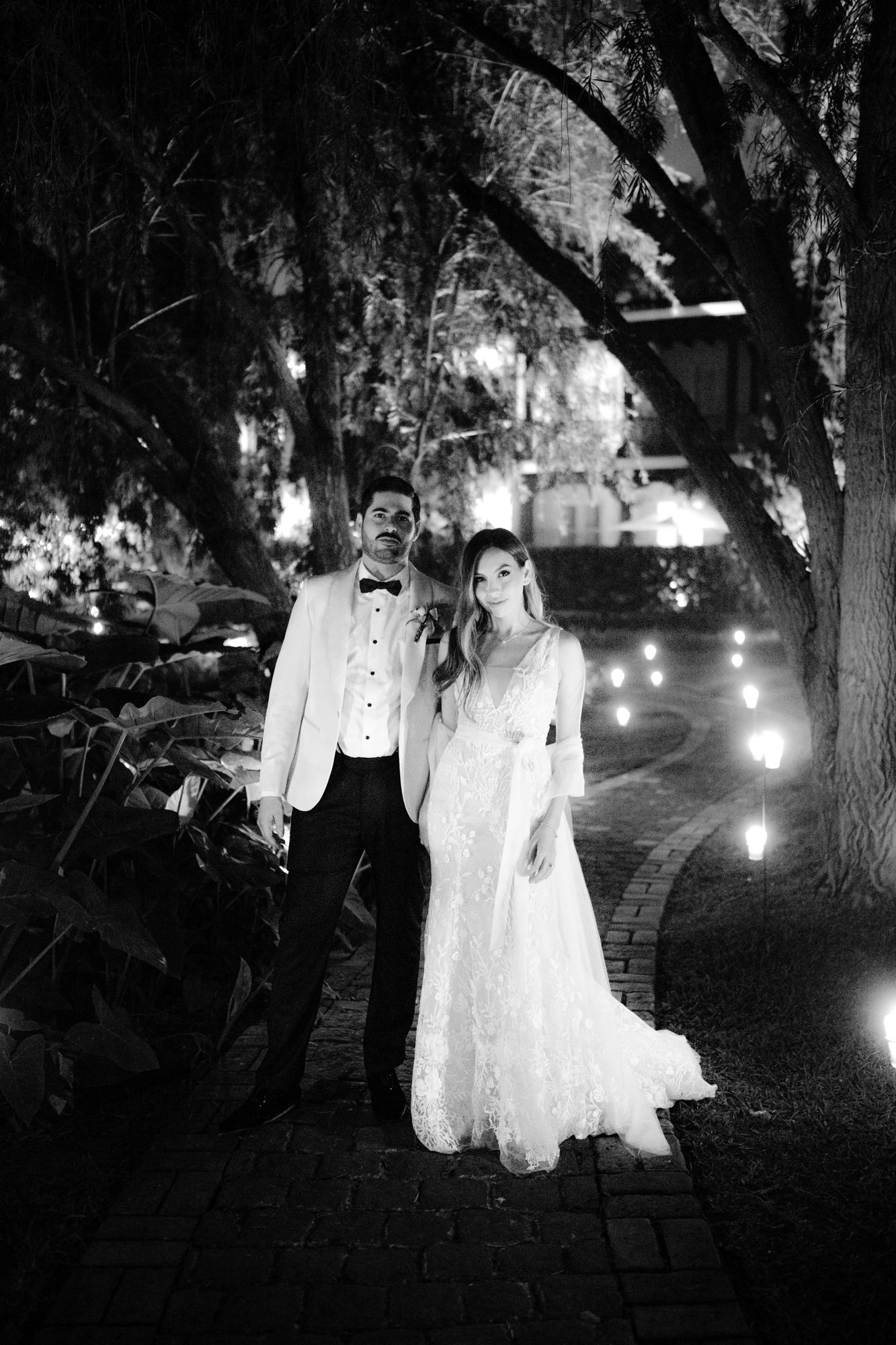 Ethereal figures in white dresses appear in a haunting nighttime scene illuminated by street lights and trees.