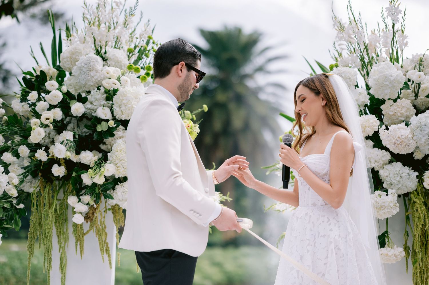 Outdoor wedding celebration with elegant white floral decorations and natural greenery.