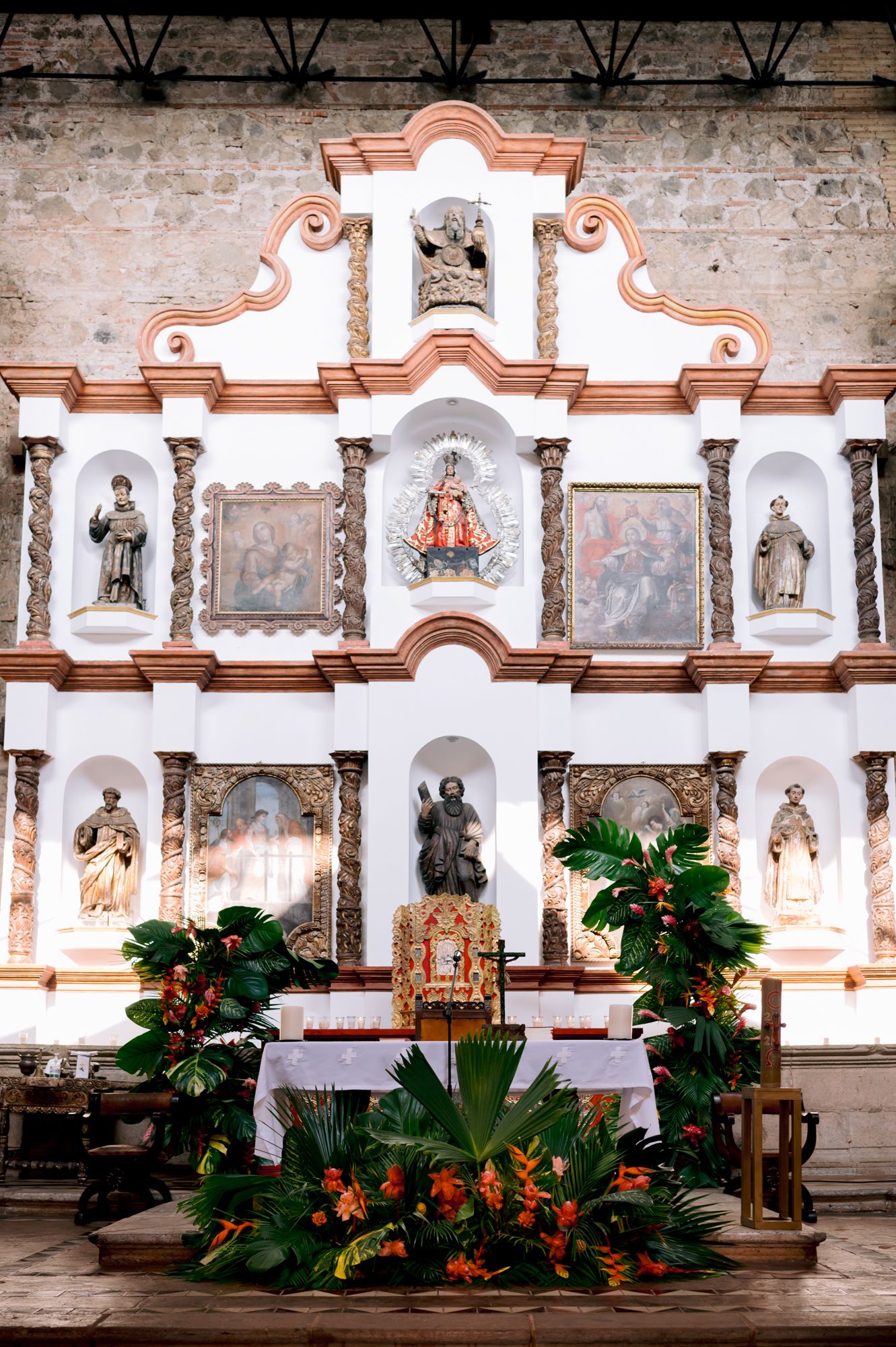 Ornate church altar decorated with tropical flowers and religious statues in colonial Spanish style.