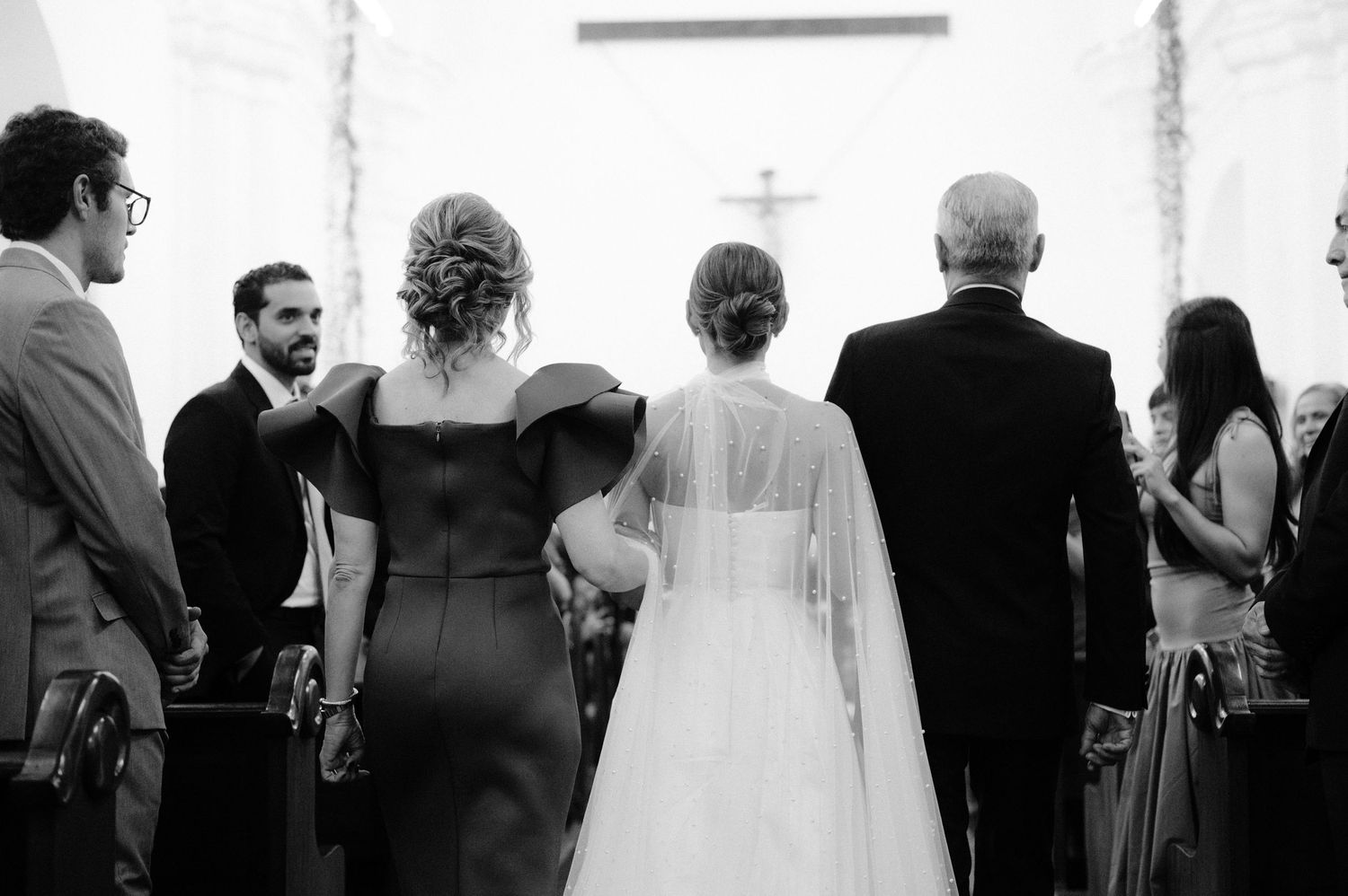 Black and white photo of wedding ceremony guests standing in church pews.