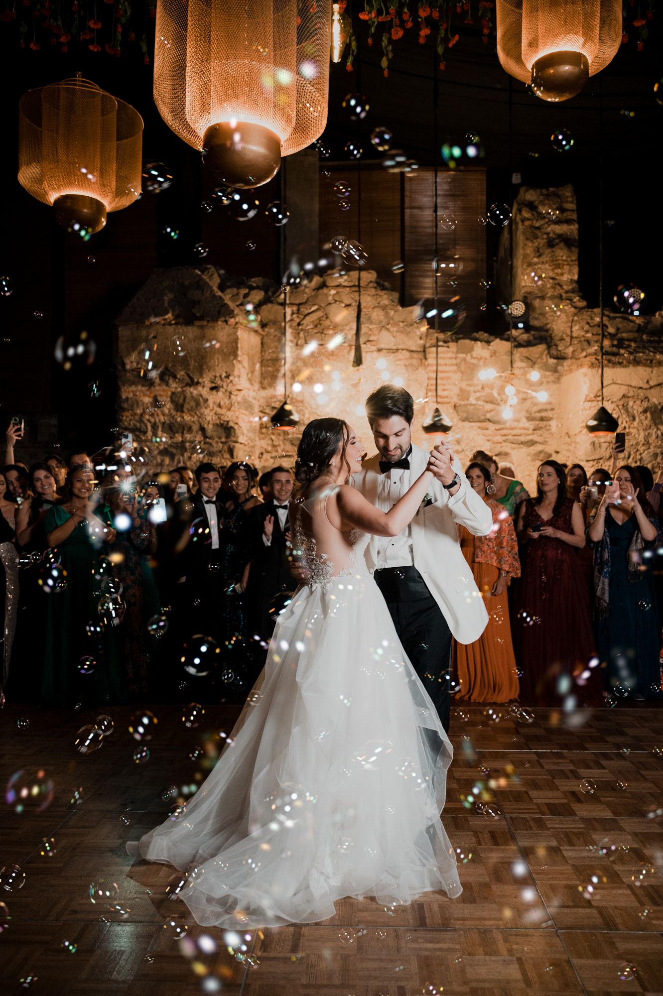 Romantic wedding dance moment with bubbles floating around couple under warm glowing lanterns.