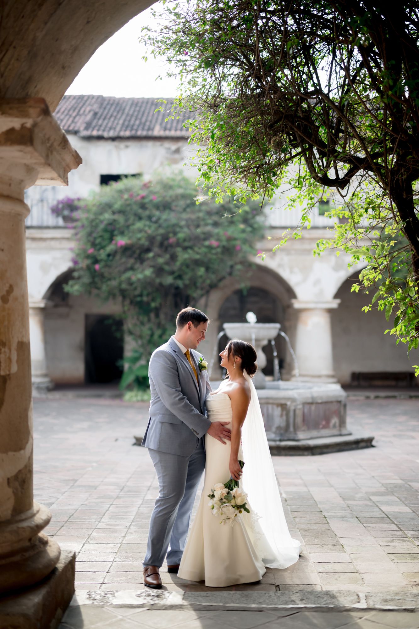 A romantic wedding portrait under stone arches in a historic courtyard with fountain.