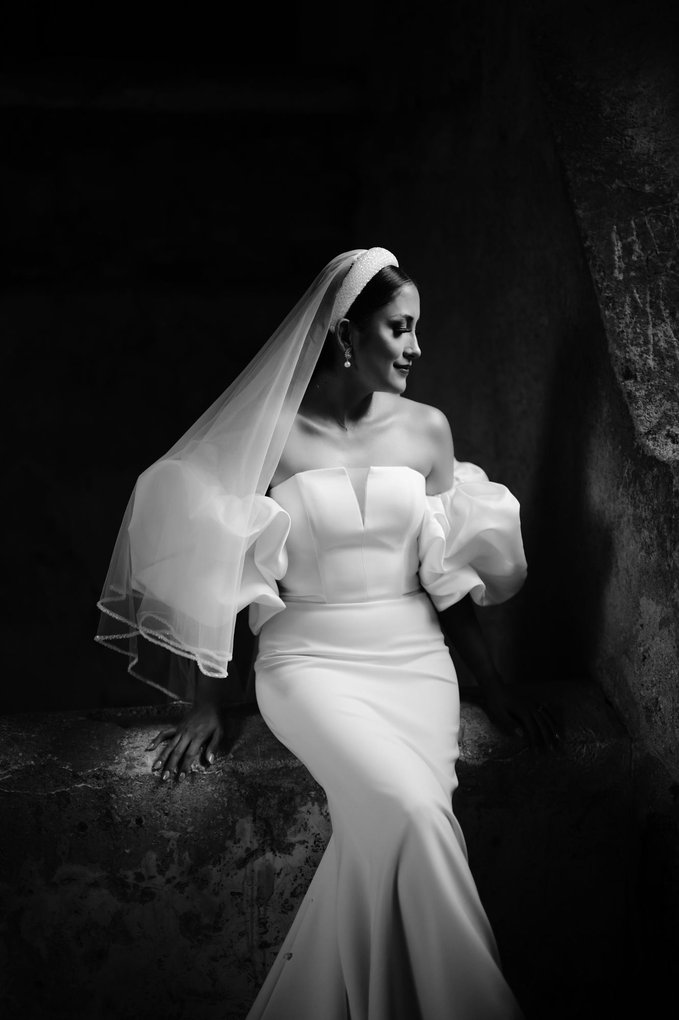 Elegant bride in fitted wedding gown with puffy sleeves and long veil poses in black and white portrait.