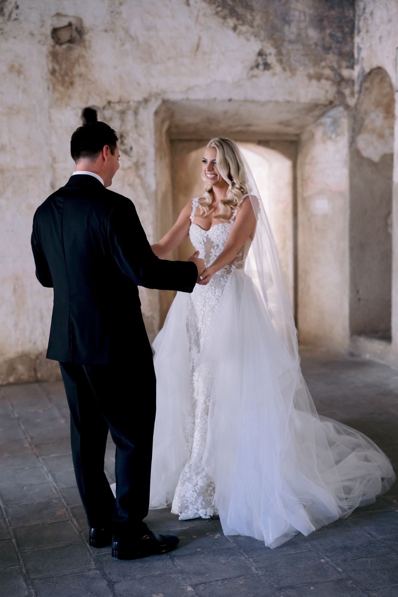 Intimate wedding portrait of couple holding hands in historic stone corridor.