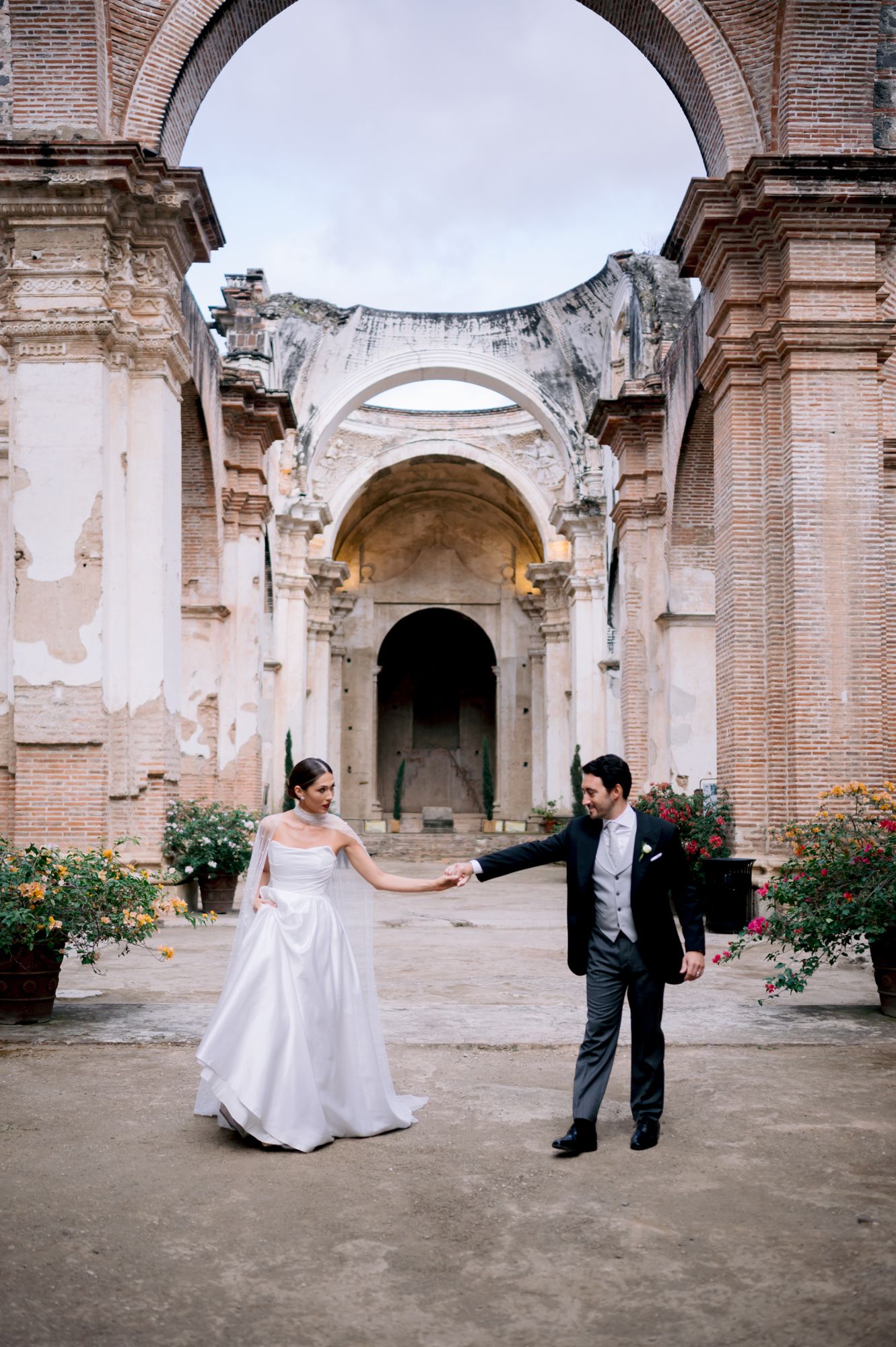 Bride and groom hold hands in romantic pose within historic church ruins.