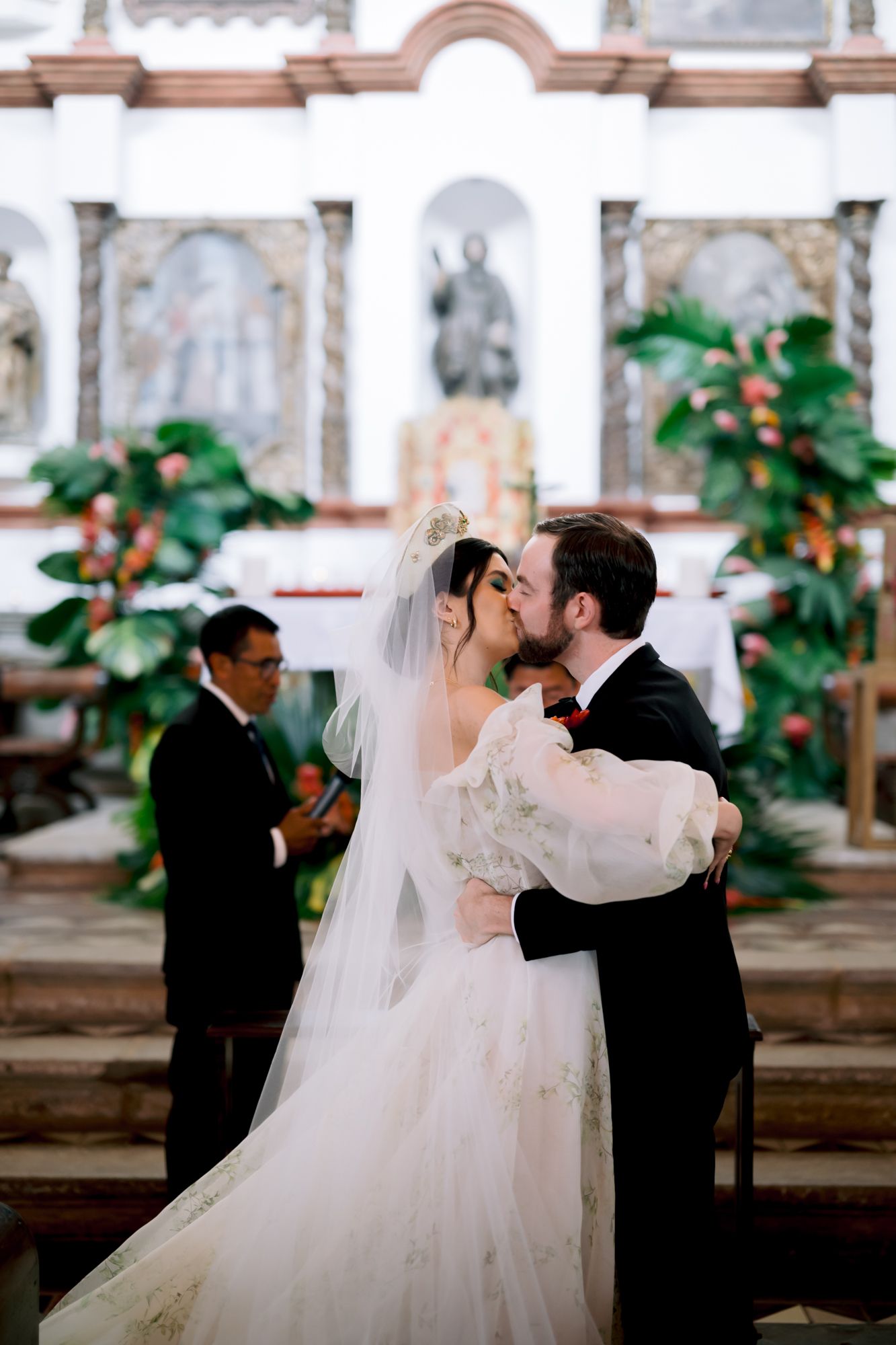 Romantic first kiss moment during a wedding ceremony in front of a decorated church altar.