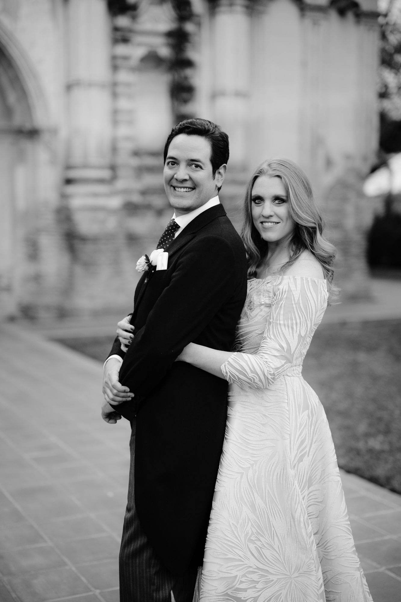 A wedding portrait of a couple in formal attire standing together against an architectural backdrop.