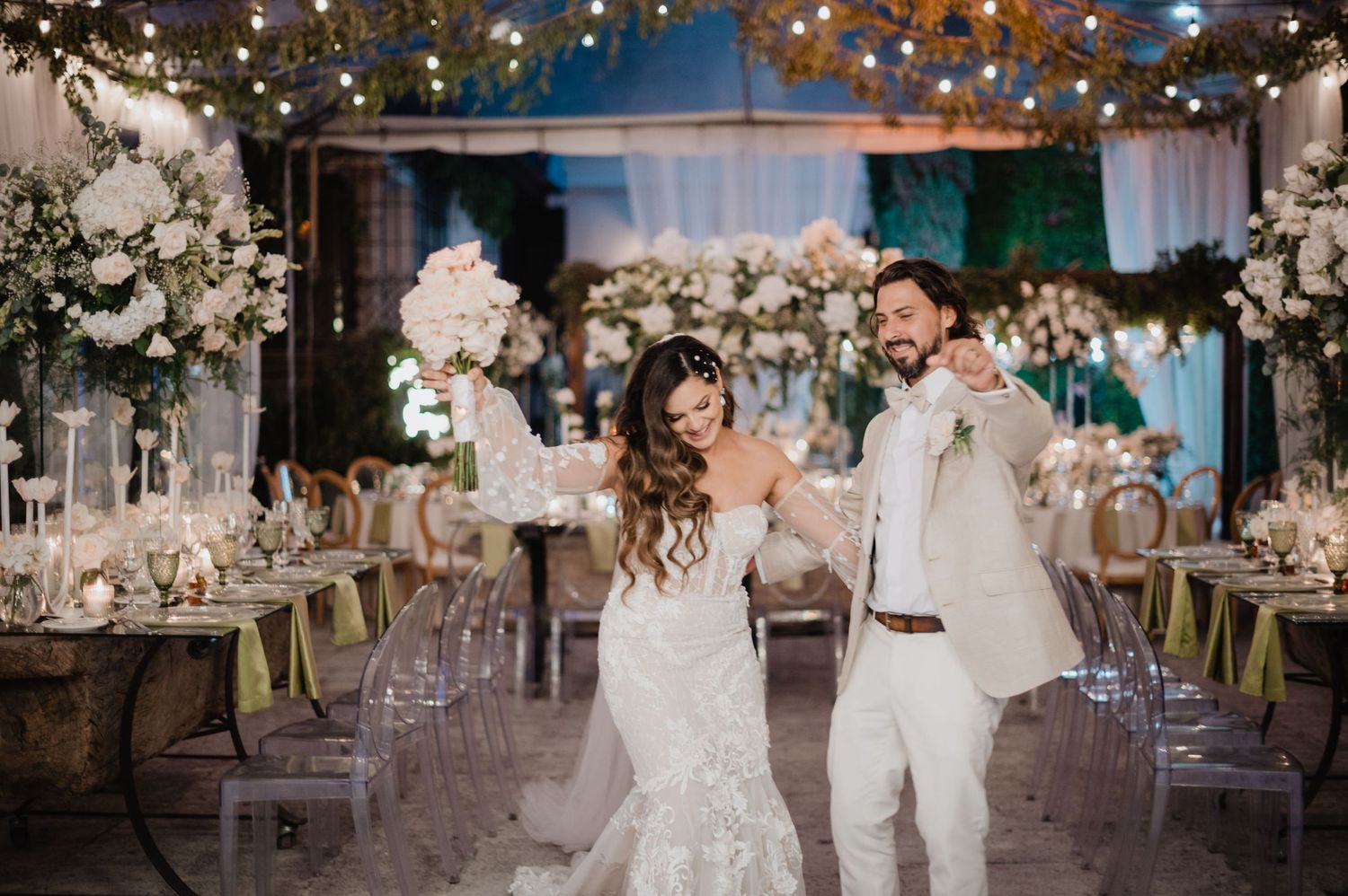 Wedding reception venue decorated with hanging lights and white floral arrangements creates magical ambiance.