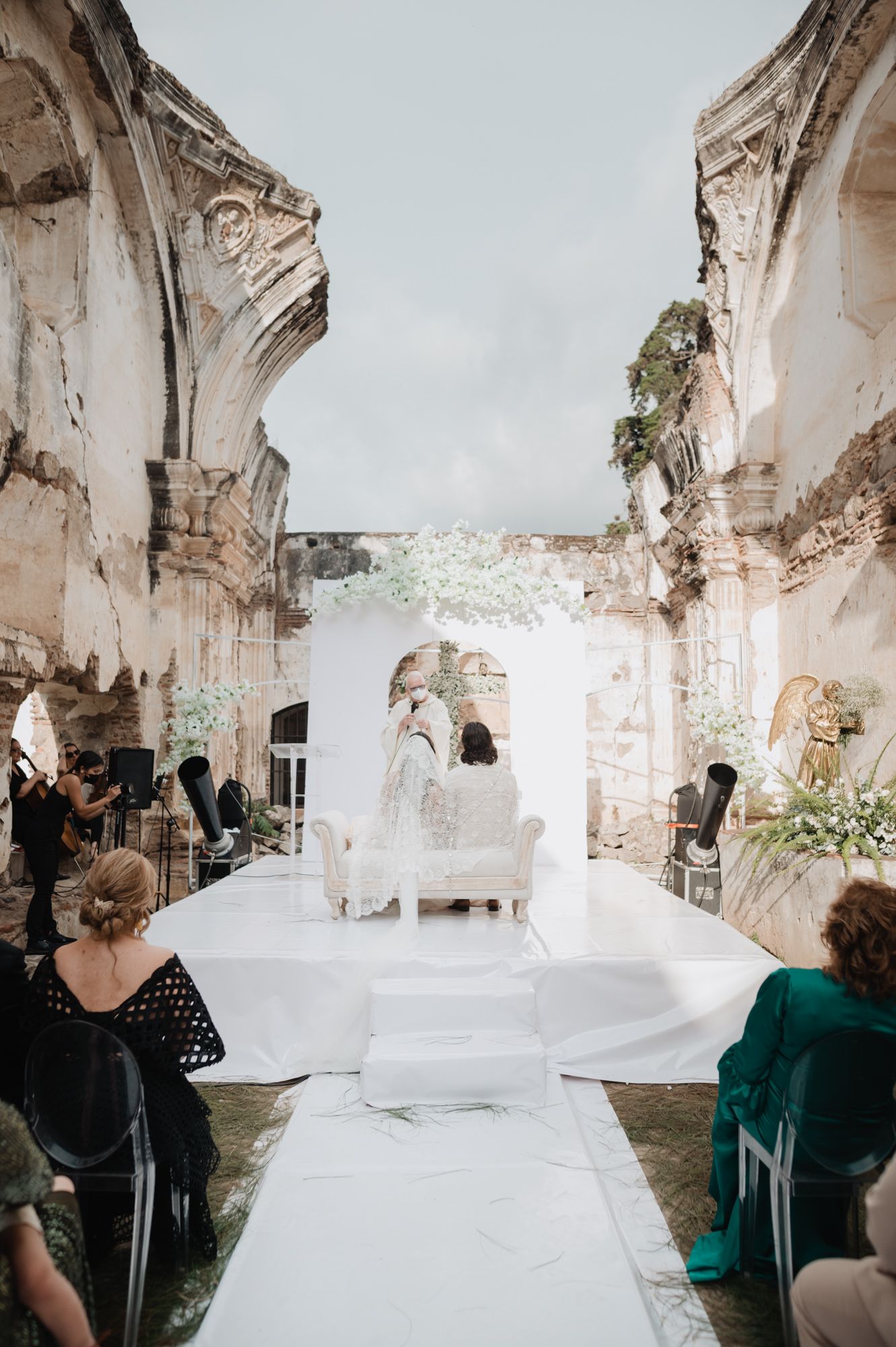 Photographers capture a wedding moment in the ruins of an ancient stone church with white flowing fabric decor.