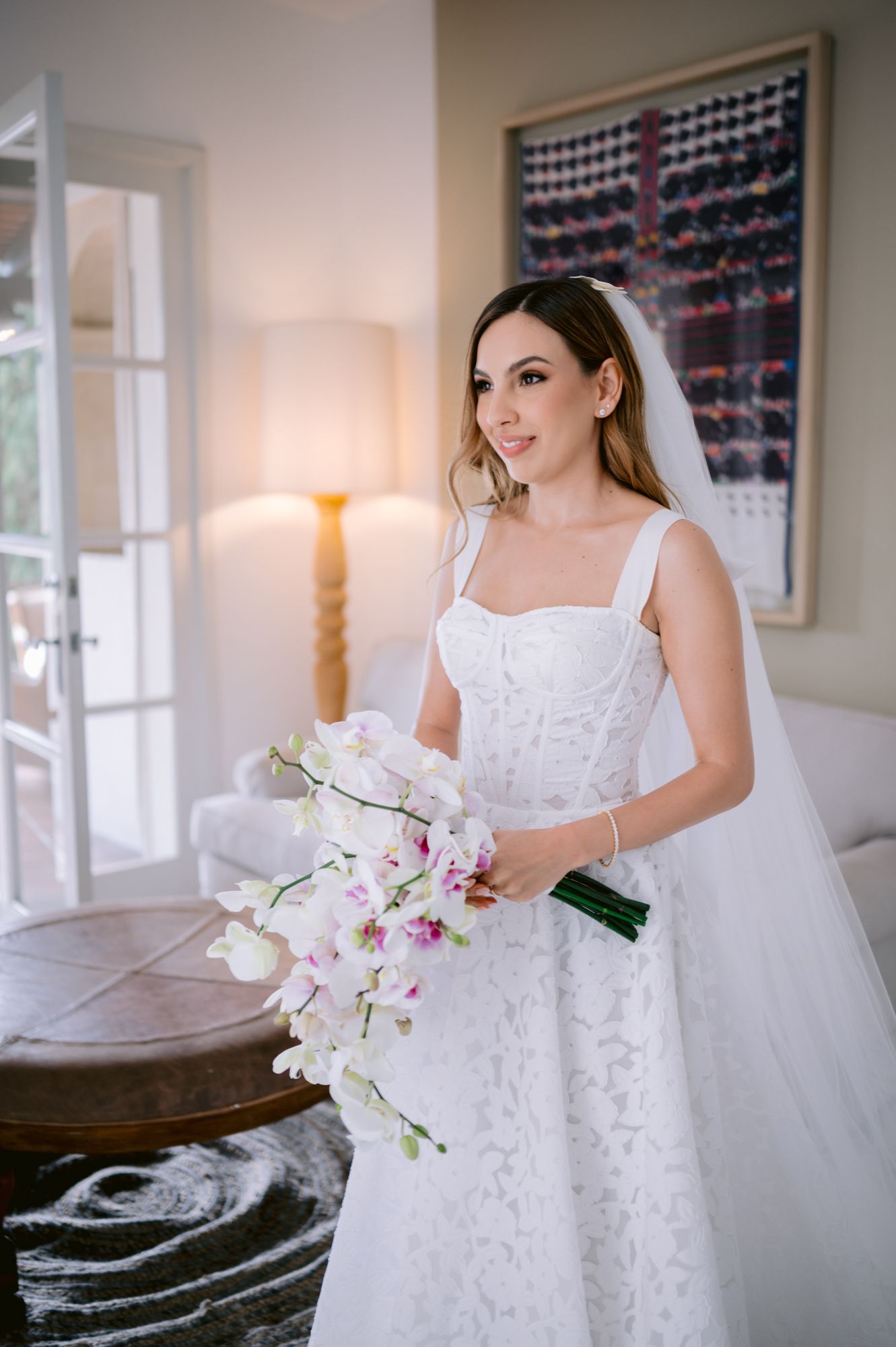 A white lace wedding dress is displayed in an elegant room with orchid flowers and soft lighting.
