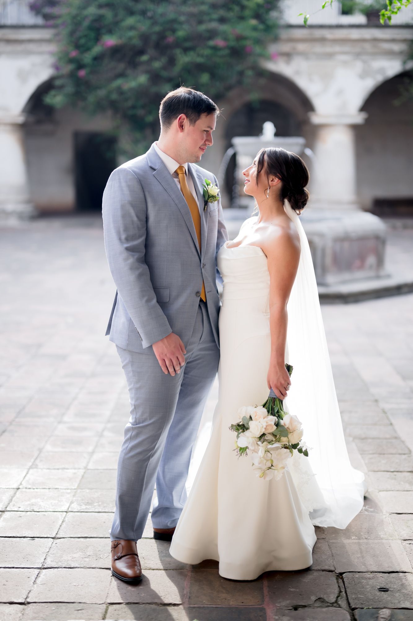 A wedding couple stands together in a Spanish colonial courtyard with stone archways.