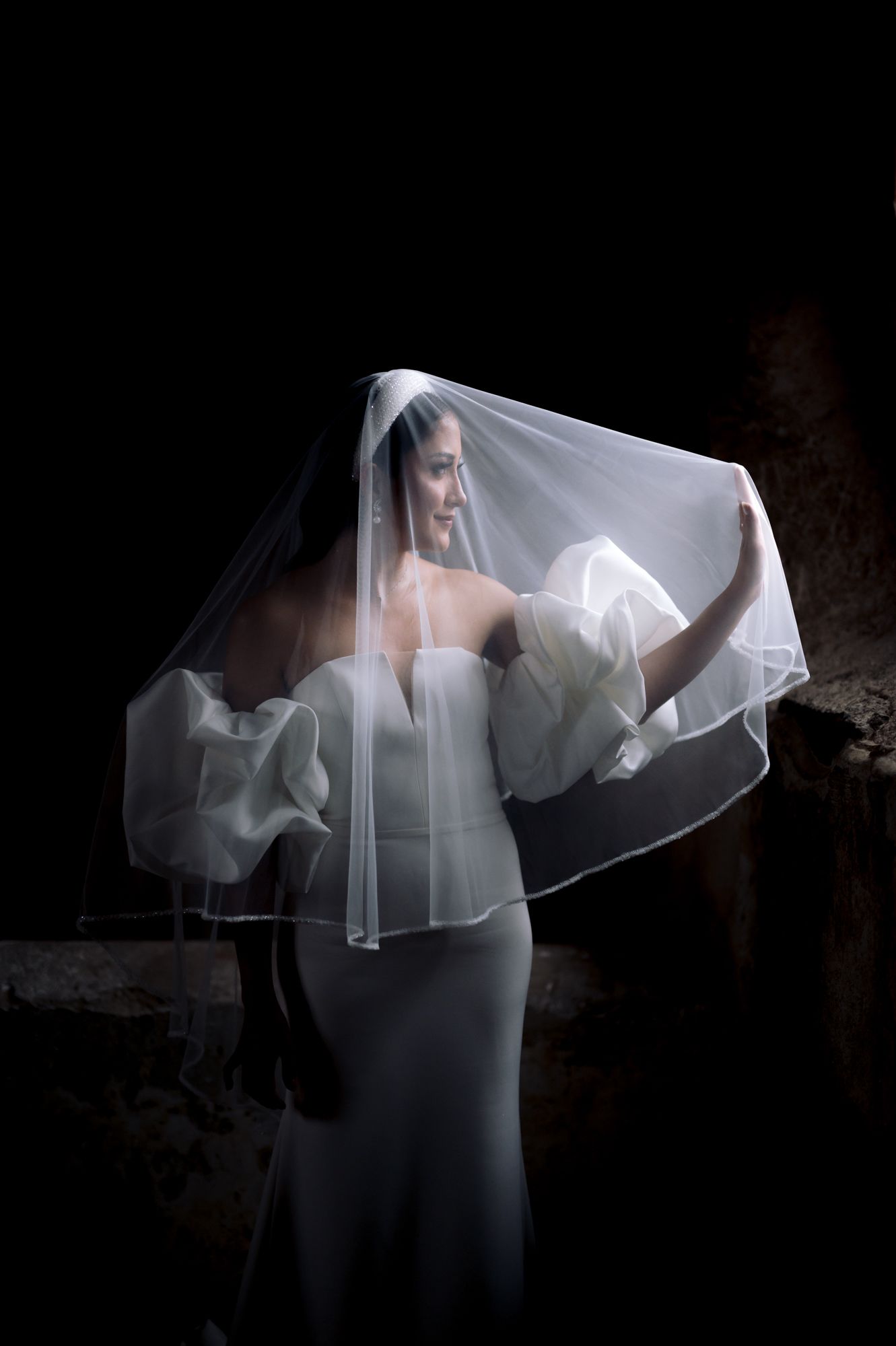 Dramatic bridal portrait featuring a flowing veil against a dark background creating an ethereal silhouette effect.