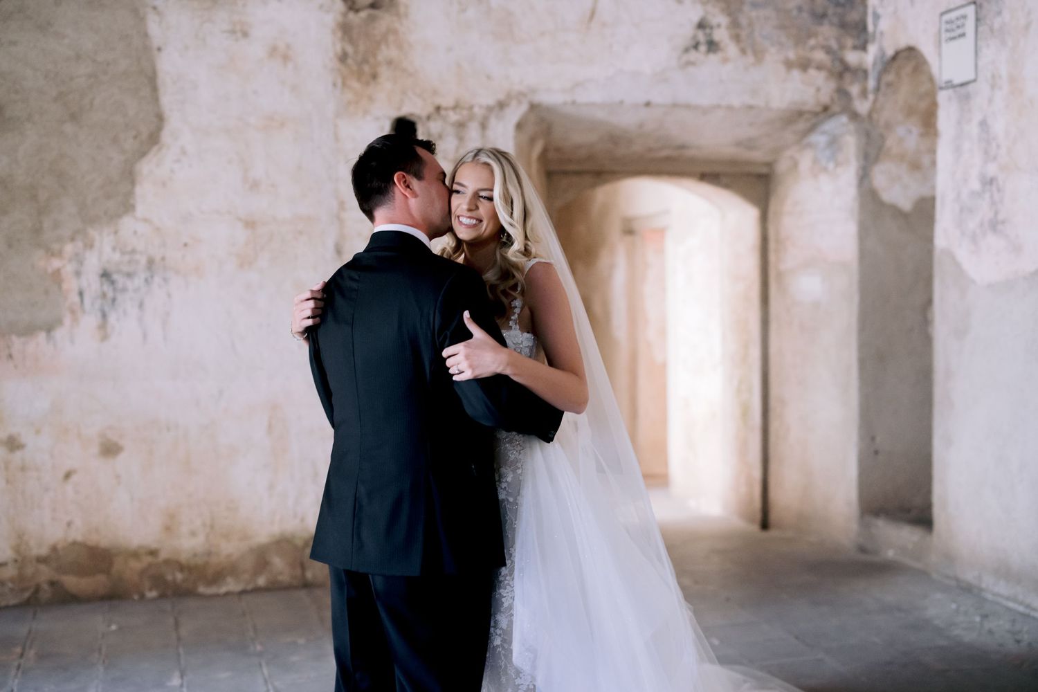 Romantic moment between newlyweds in historic stone venue with natural lighting.