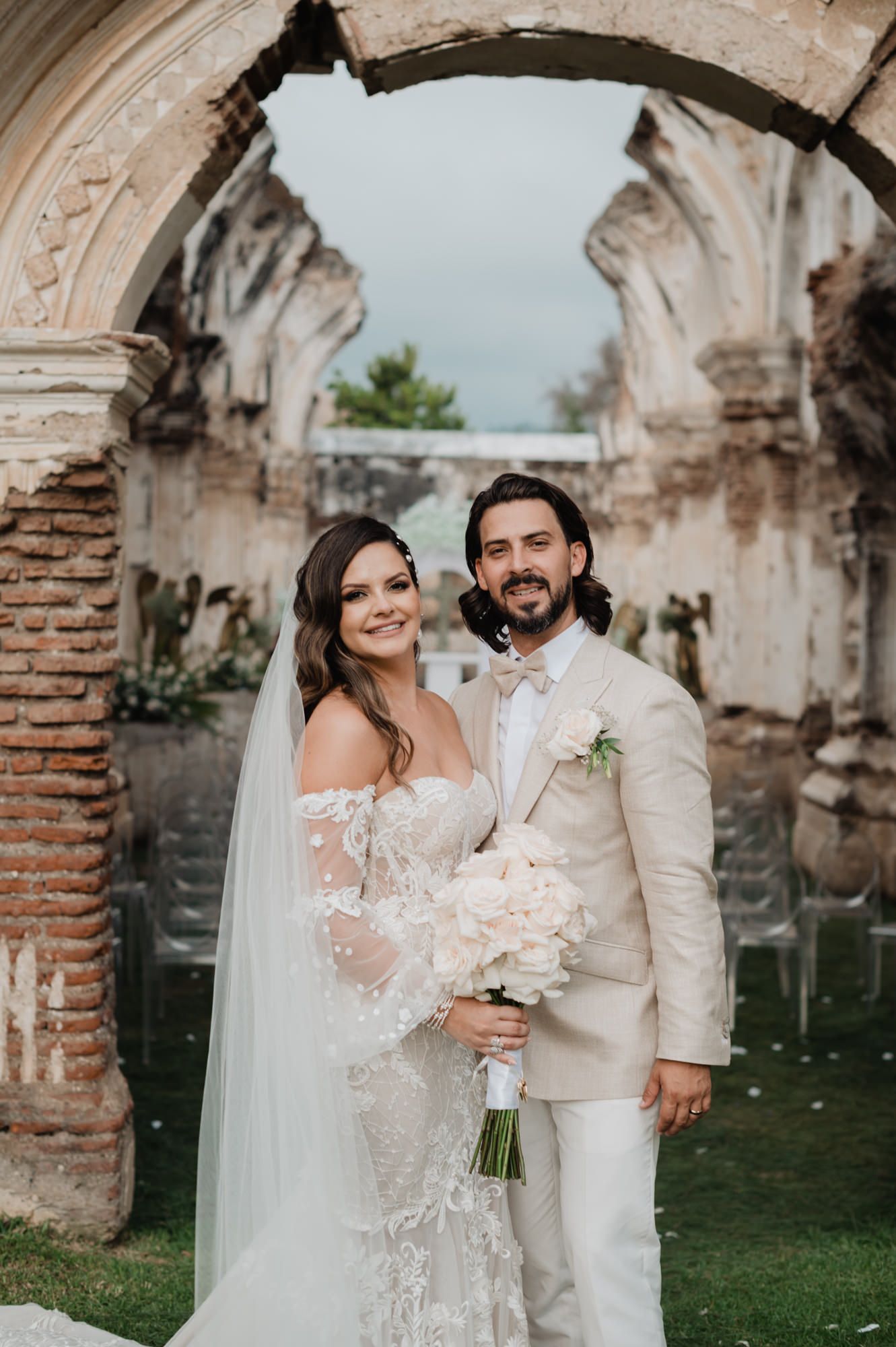 Elegant wedding couple embraces in front of ancient stone ruins with beautiful natural lighting.