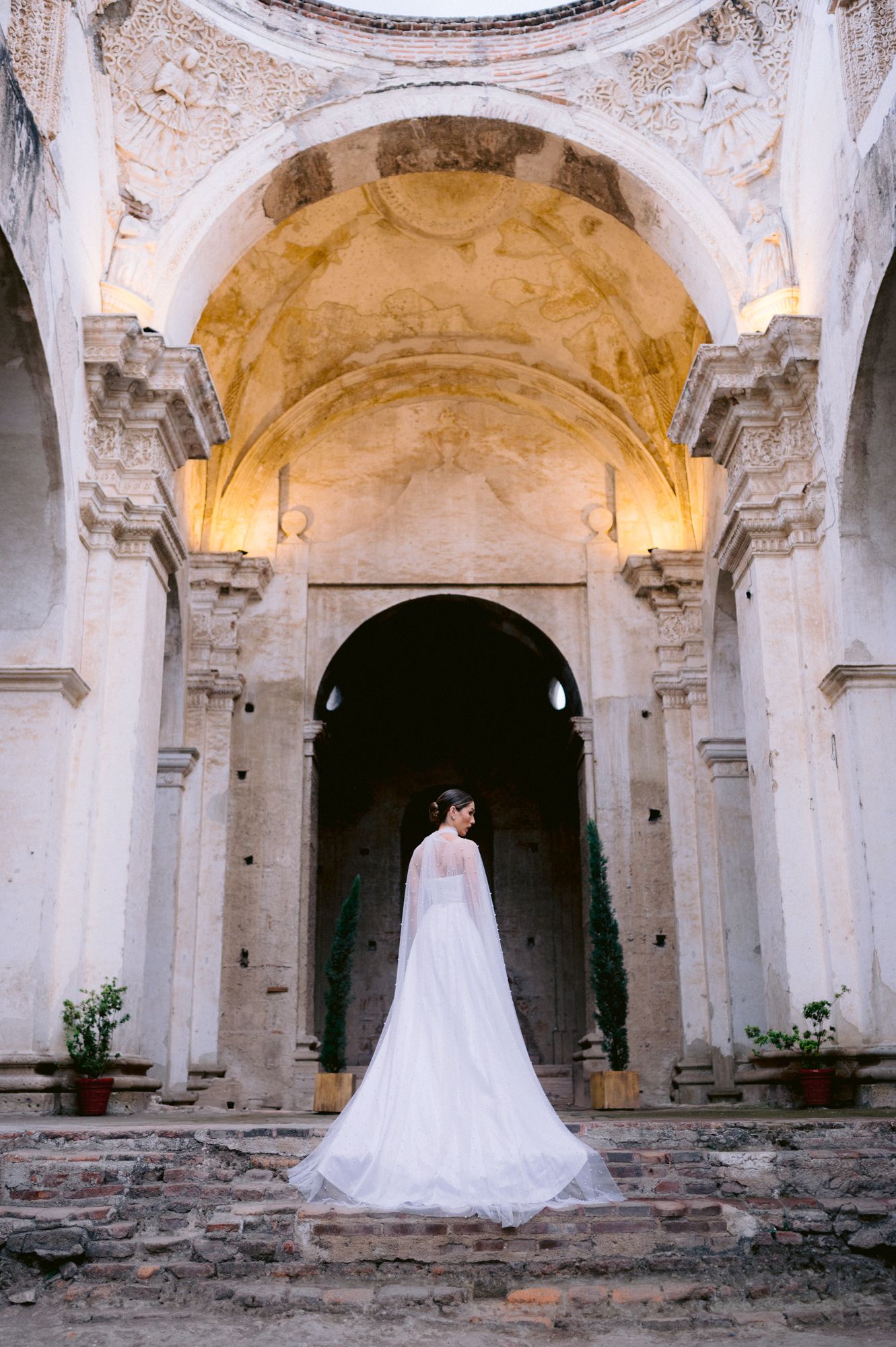 Wedding dress with flowing train captured in historic church archway with golden dome ceiling.