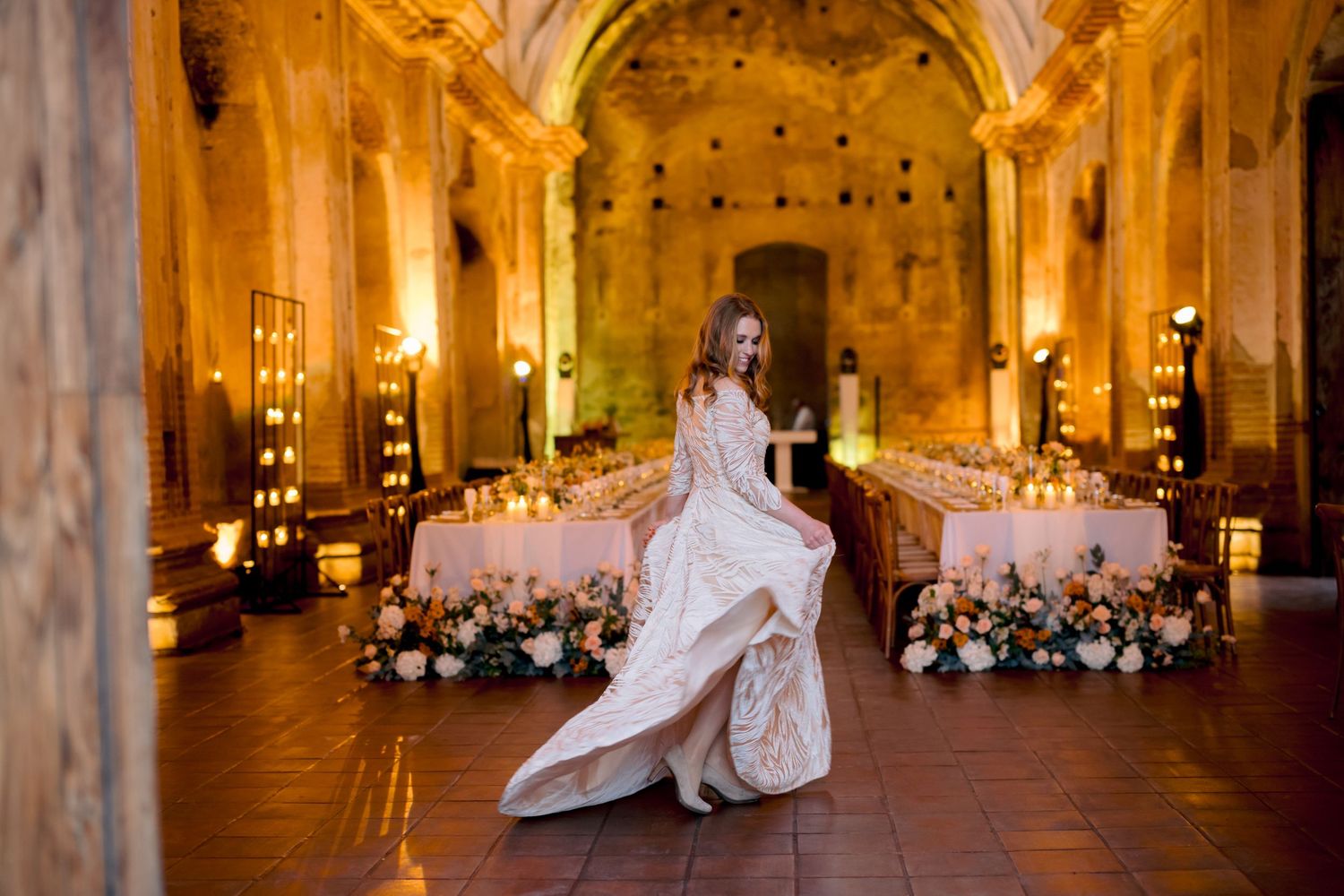 Bride twirls in elegant white gown in ornate reception hall with candlelit tables.