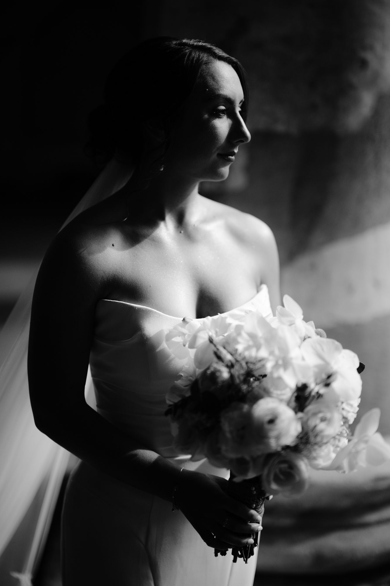 Artistic black and white bridal portrait with dramatic side lighting and white bouquet.