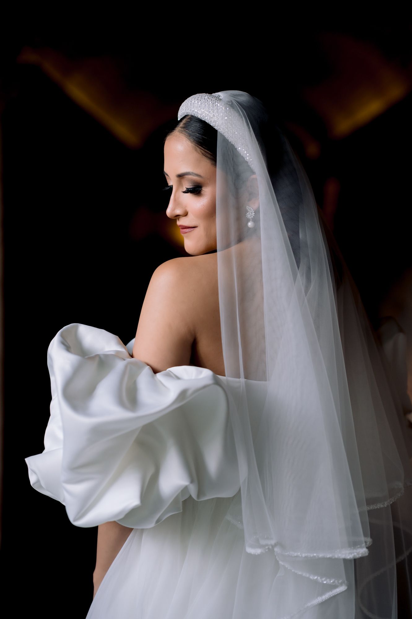 Artistic profile shot of bride in white wedding gown with delicate veil against dark background.