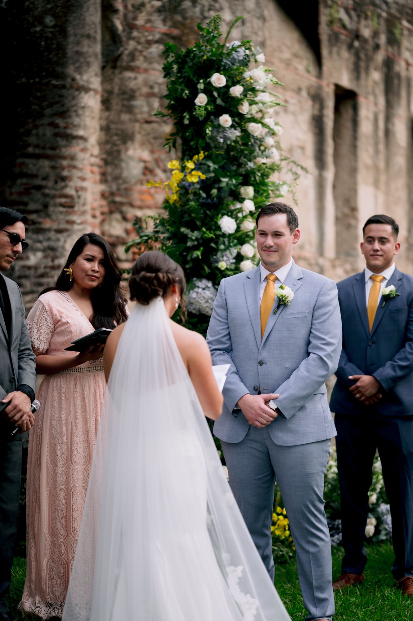 Wedding ceremony in progress against backdrop of historic brick ruins with floral decorations.