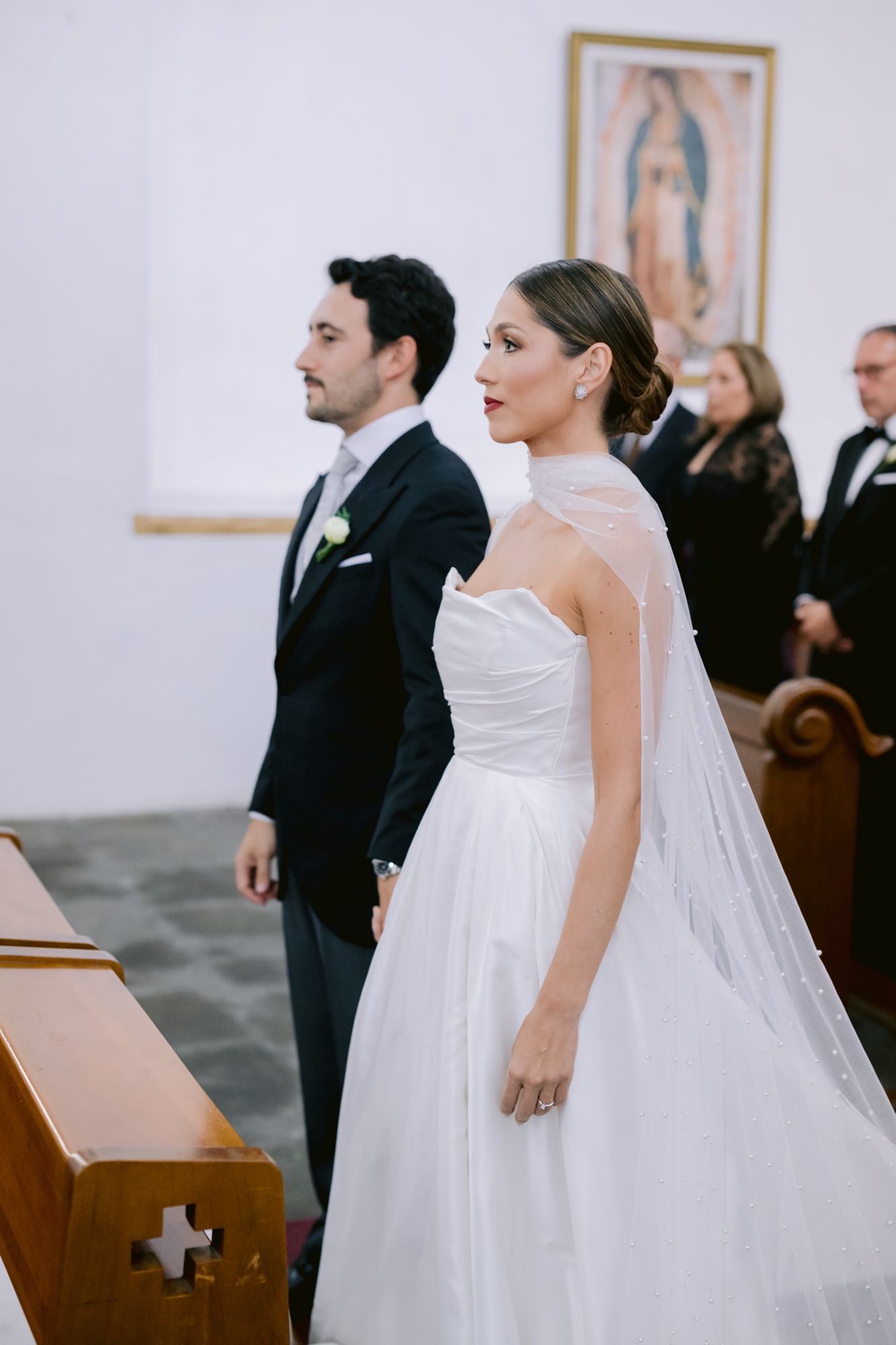 Bride in classic white gown and groom in dark suit standing at church altar during ceremony.