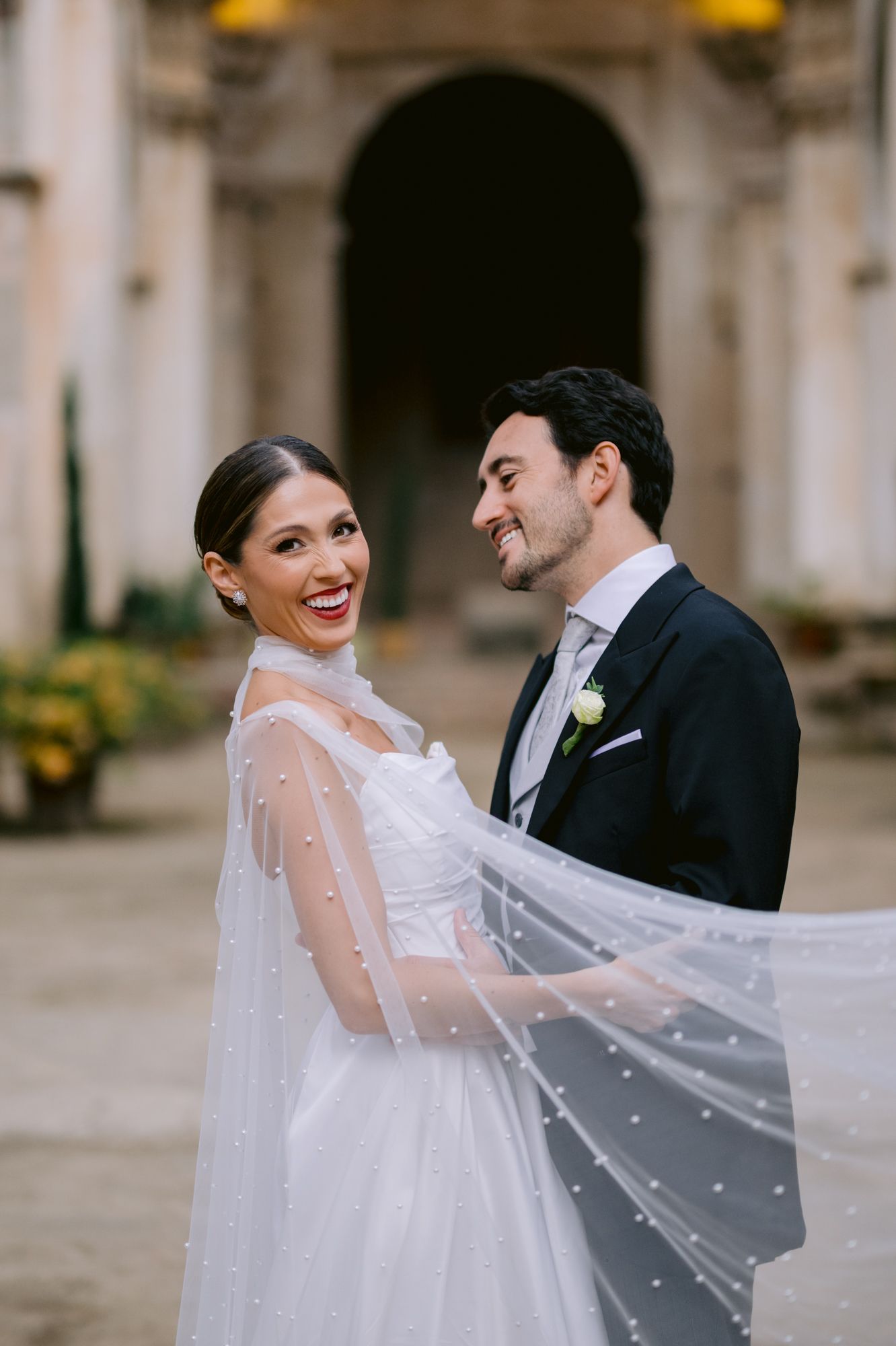 Joyful wedding couple shares a candid moment while wrapped in delicate tulle veil.