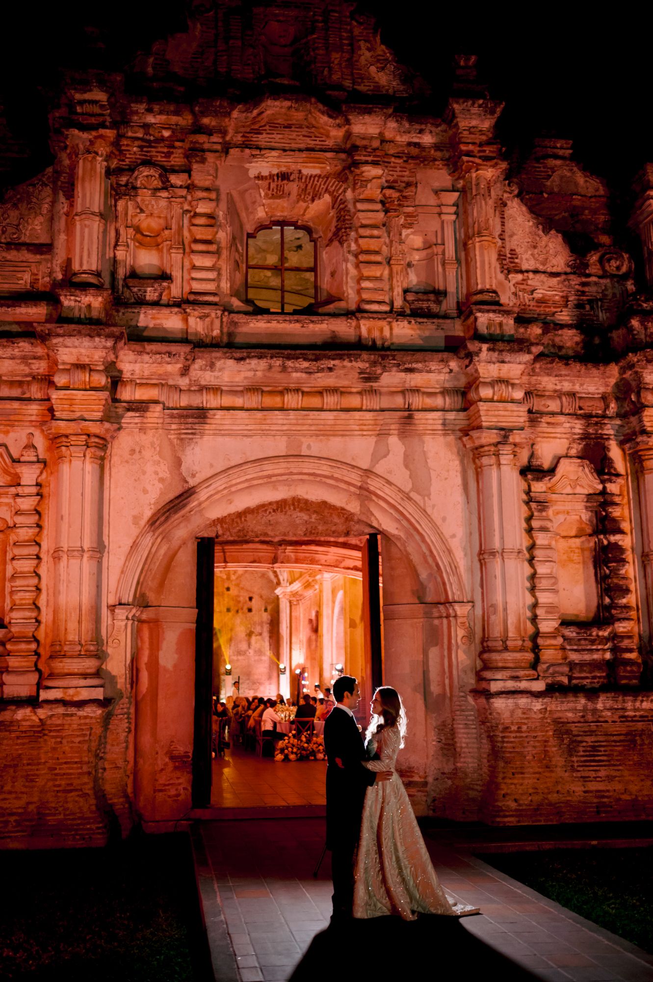 Silhouetted couple in doorway of illuminated ancient stone church at night.