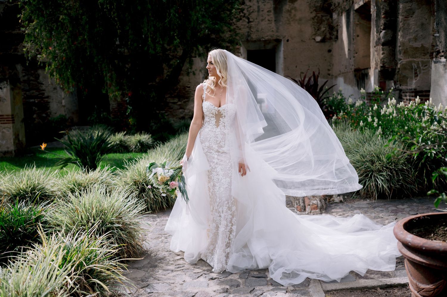 A wedding themed photo series set in an elegant outdoor garden venue with flowing white gowns and romantic veils.